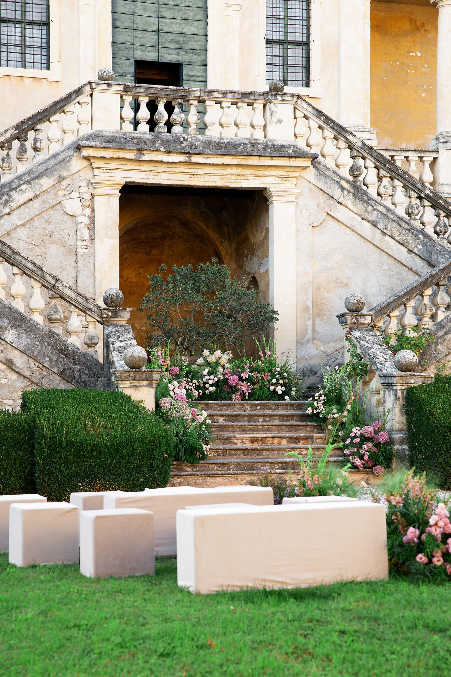 Elegant stone staircase adorned with flowering plants and modern concrete benches at a historic European villa entrance.