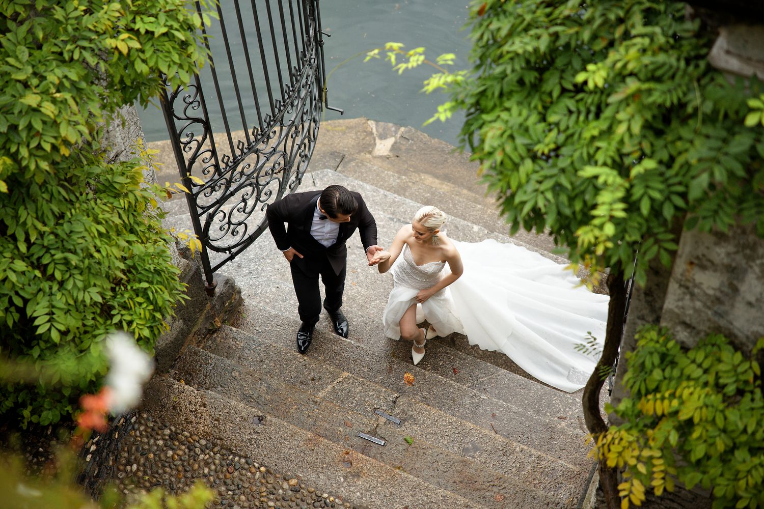 Elegant couple descending stone steps surrounded by wrought iron railings and green foliage.