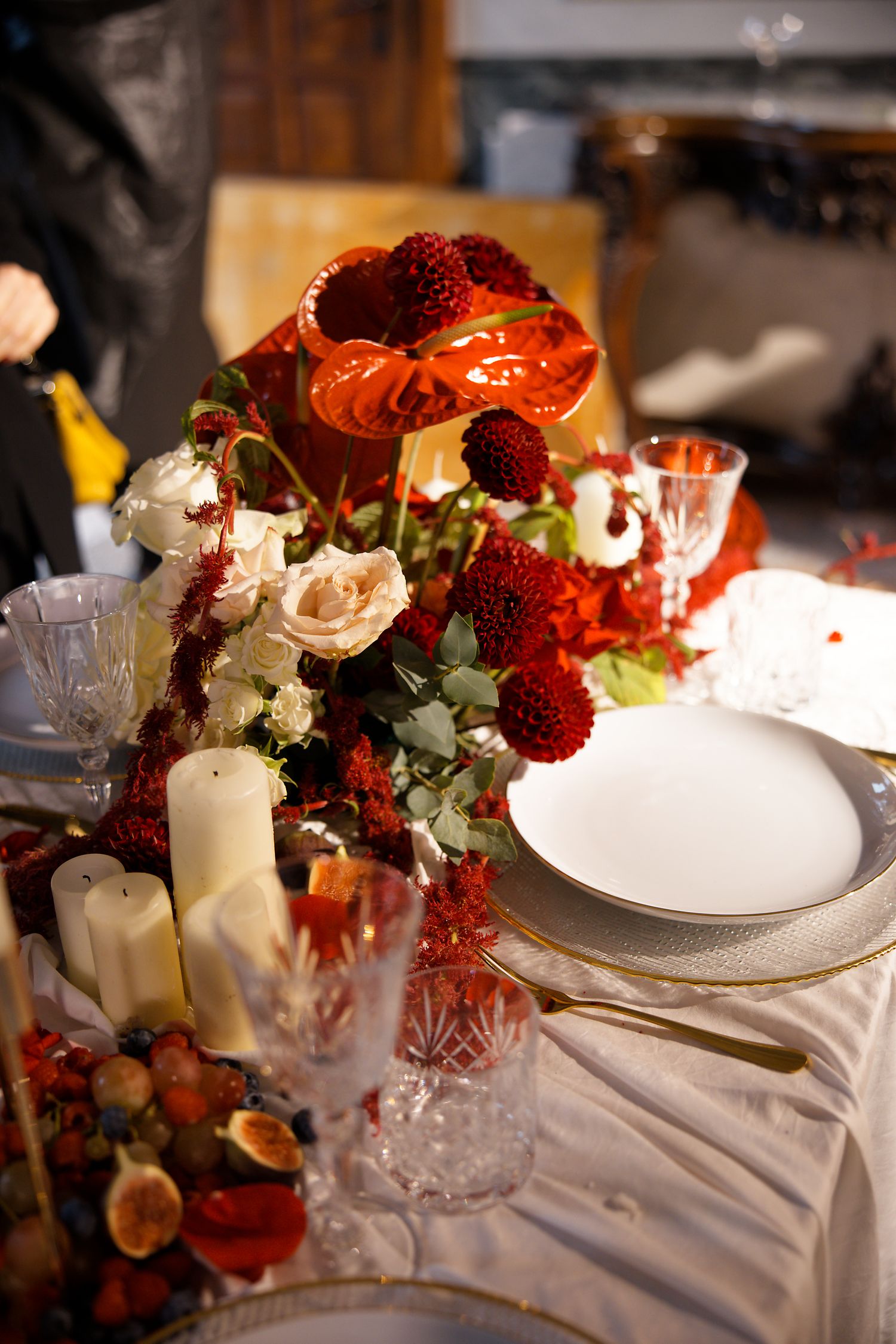 Elegant wedding table centerpiece with red flowers, roses, and crystal glassware on white linens.