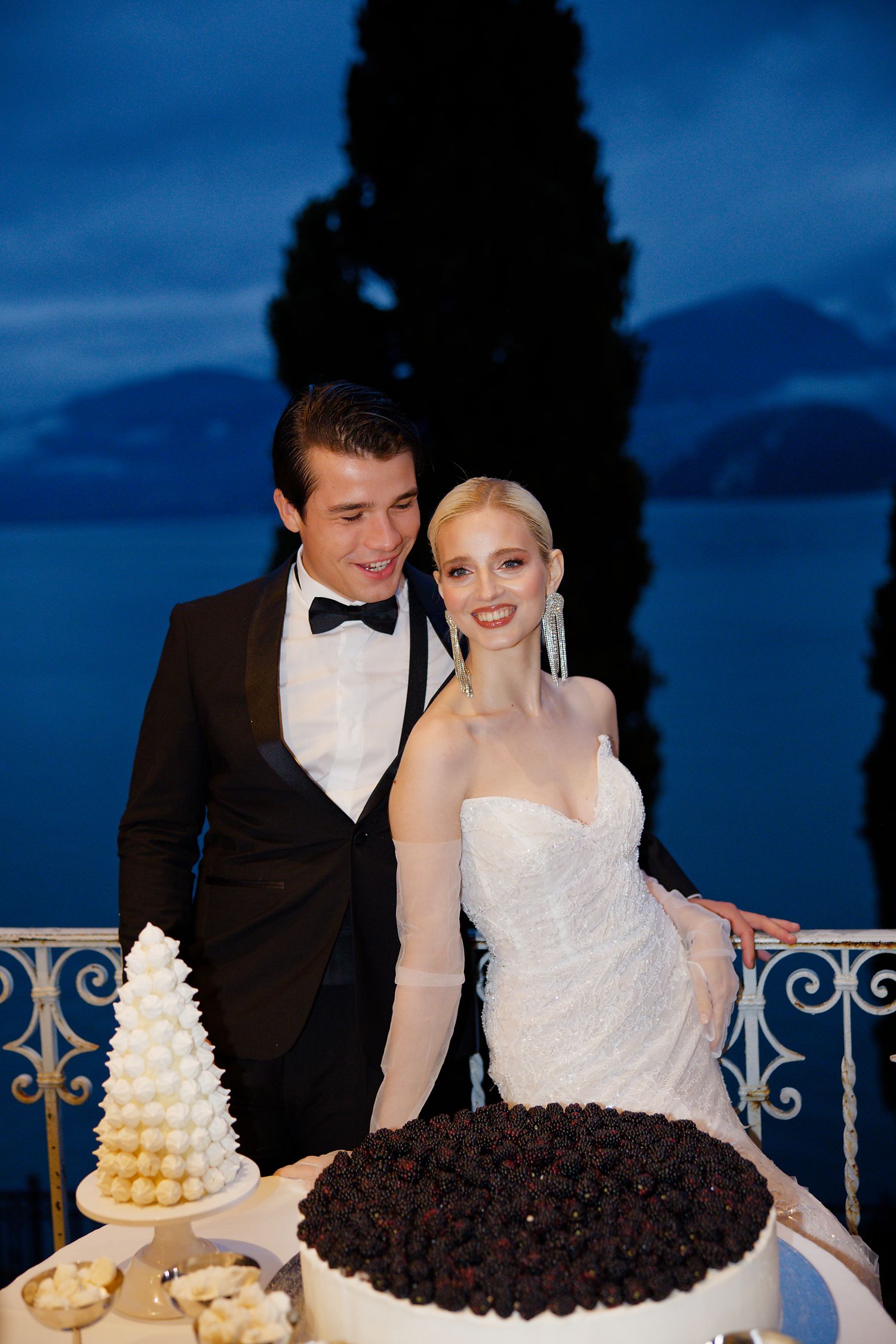 Newlyweds share an intimate moment beside their wedding cake with mountain views in the background.