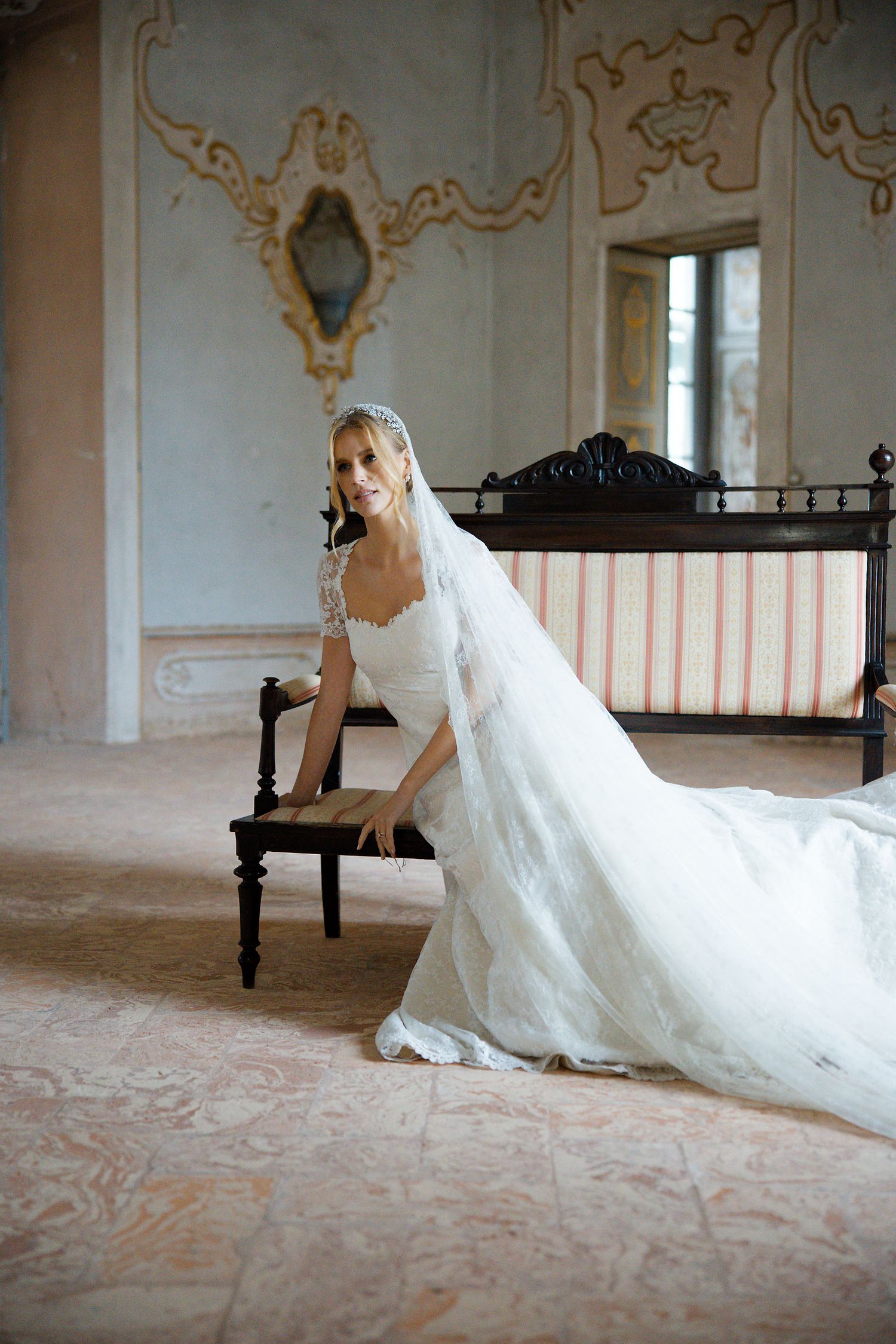 A white gown flows elegantly across pink marble floors in an ornate historic room.