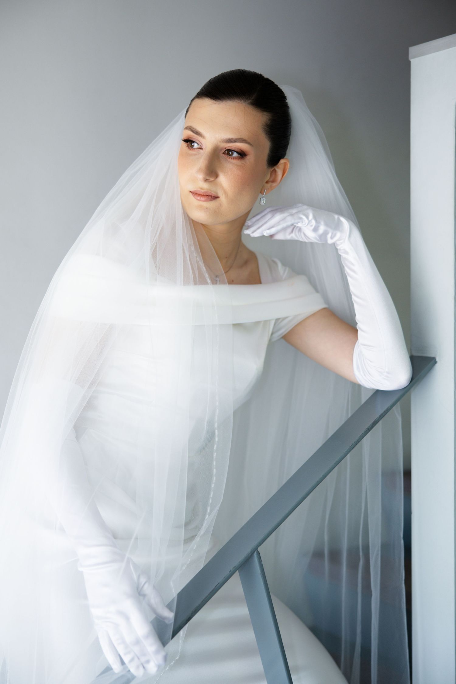 Artistic series of a bride in white dress and veil leaning against a gray wall.