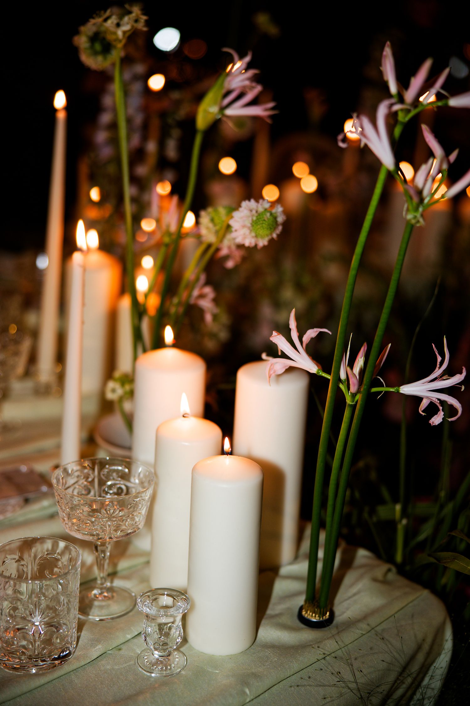 Elegant table setting with white candles and lilies for evening wedding reception.