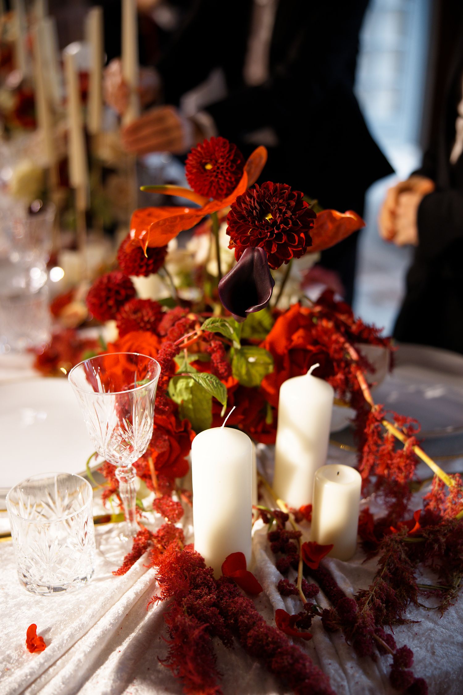 Romantic table setting with red florals, crystal glasses and white candles creating an elegant atmosphere.