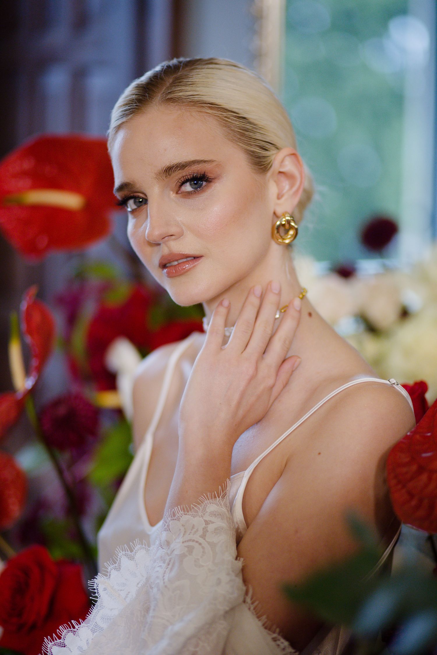 A bride in lace shows off her engagement ring among red roses.