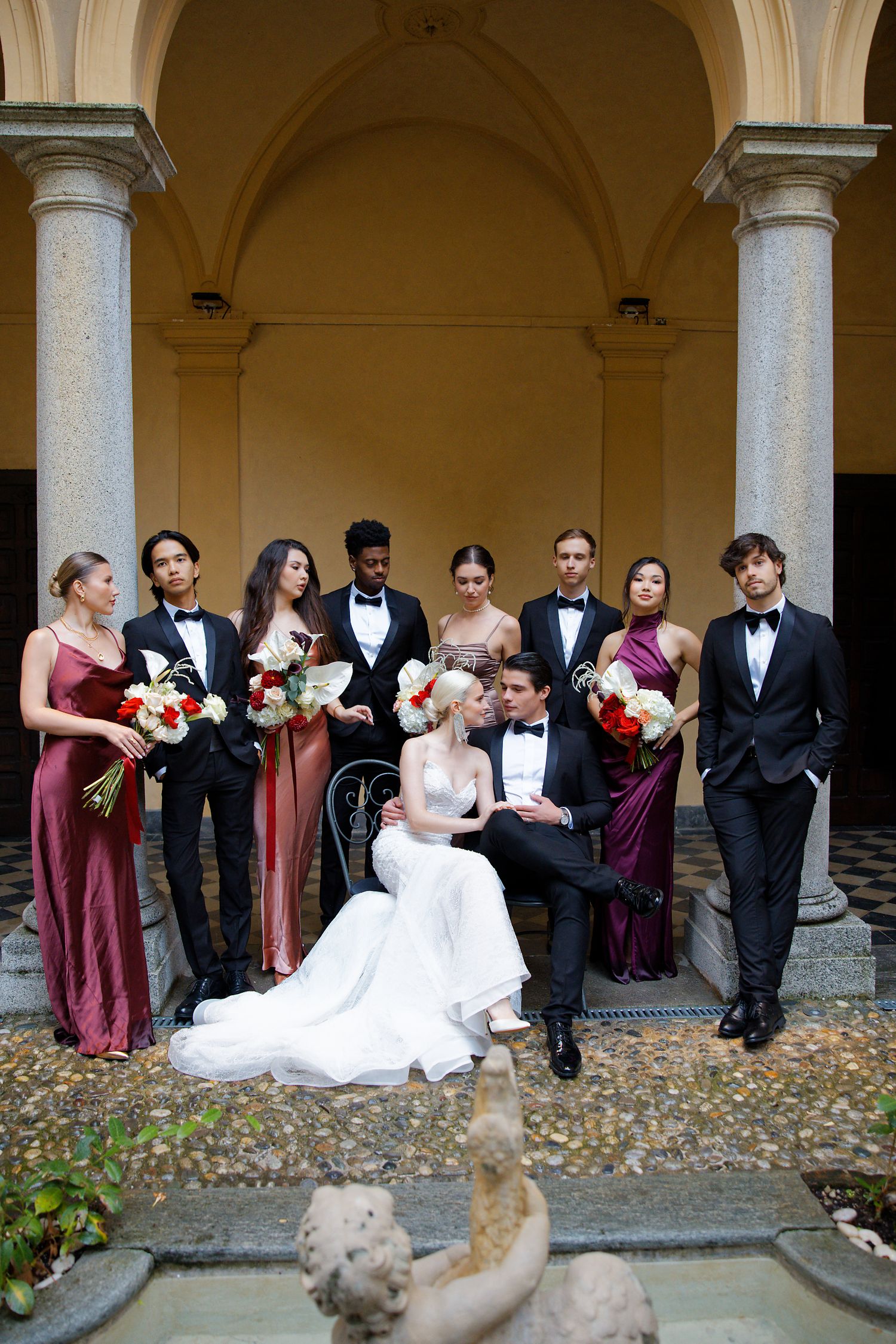 Wedding party in formal attire posing under an ornate archway with classic architecture.