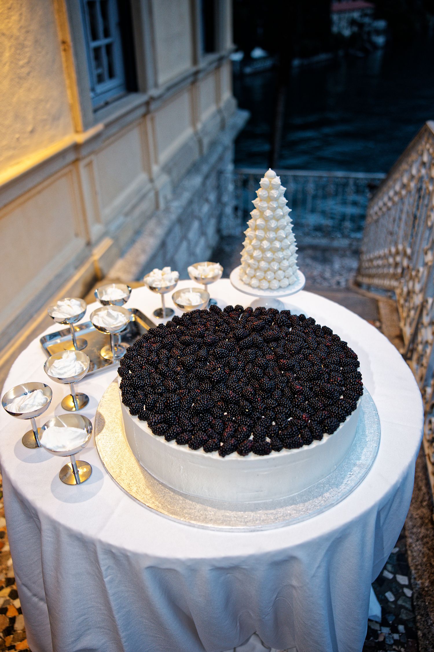 Wedding cake table features white kransekake tower and dark chocolate covered dessert on white tablecloth.