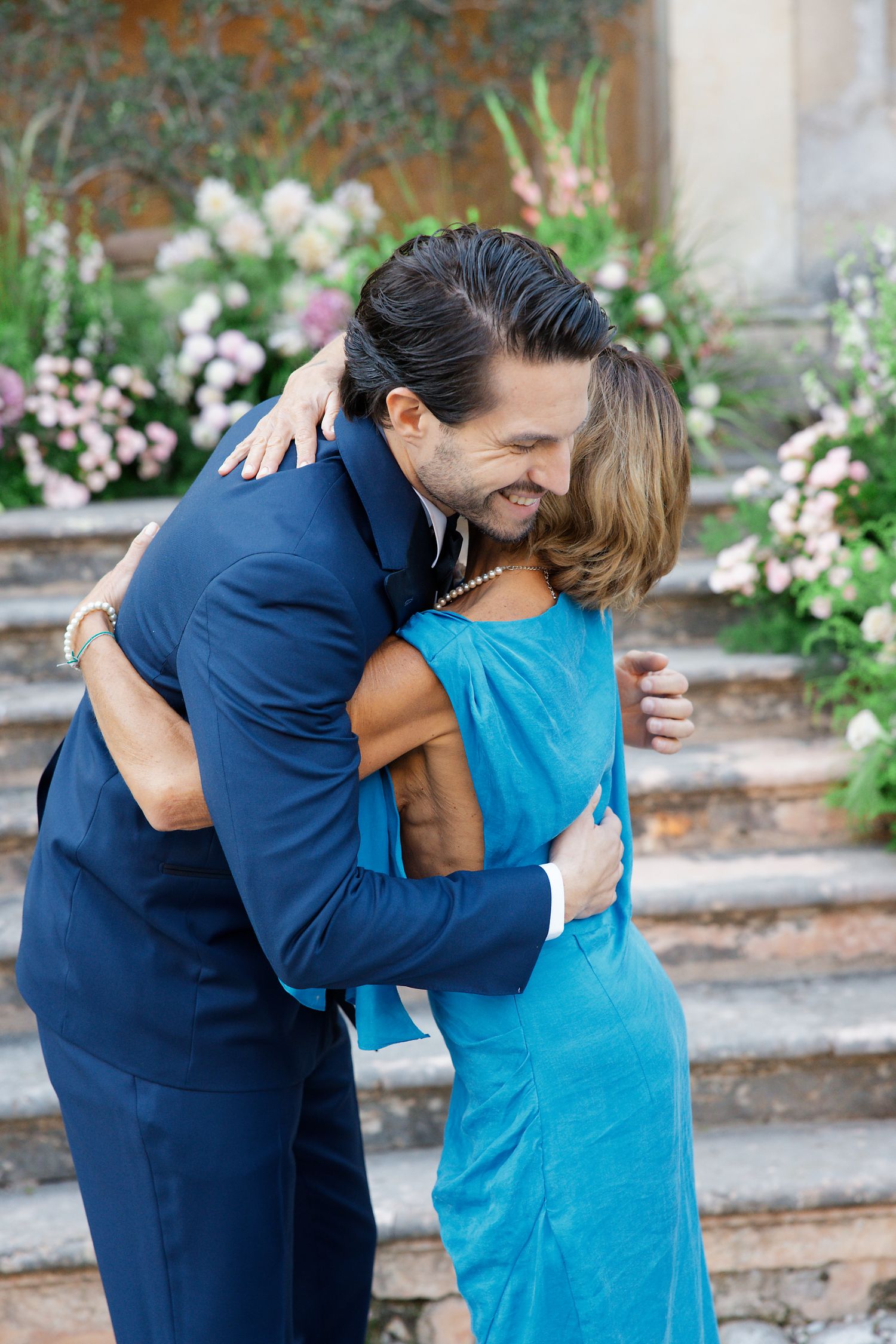 Emotional embrace shared on garden steps surrounded by blooming flowers.