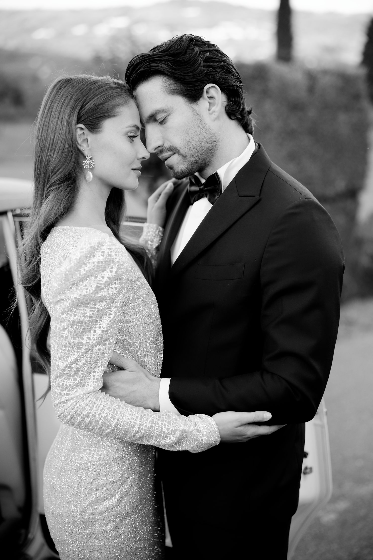 Romantic black and white portrait of couple in formal attire embracing.