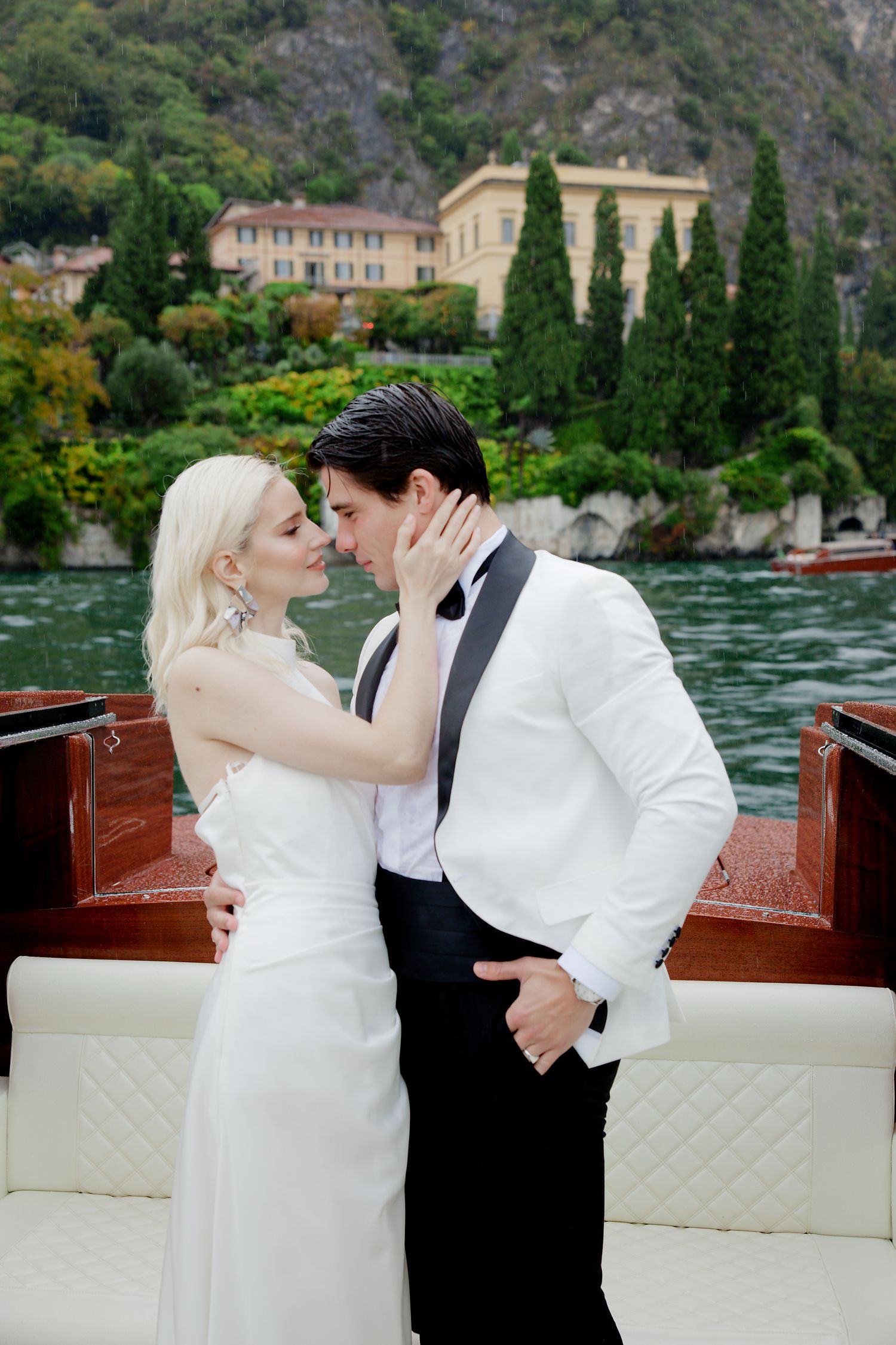 Romantic moment between newlyweds on wooden boat with Italian villa backdrop.