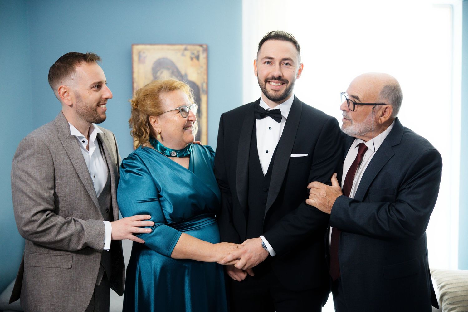 Wedding guests in formal attire greeting each other warmly at an indoor venue.