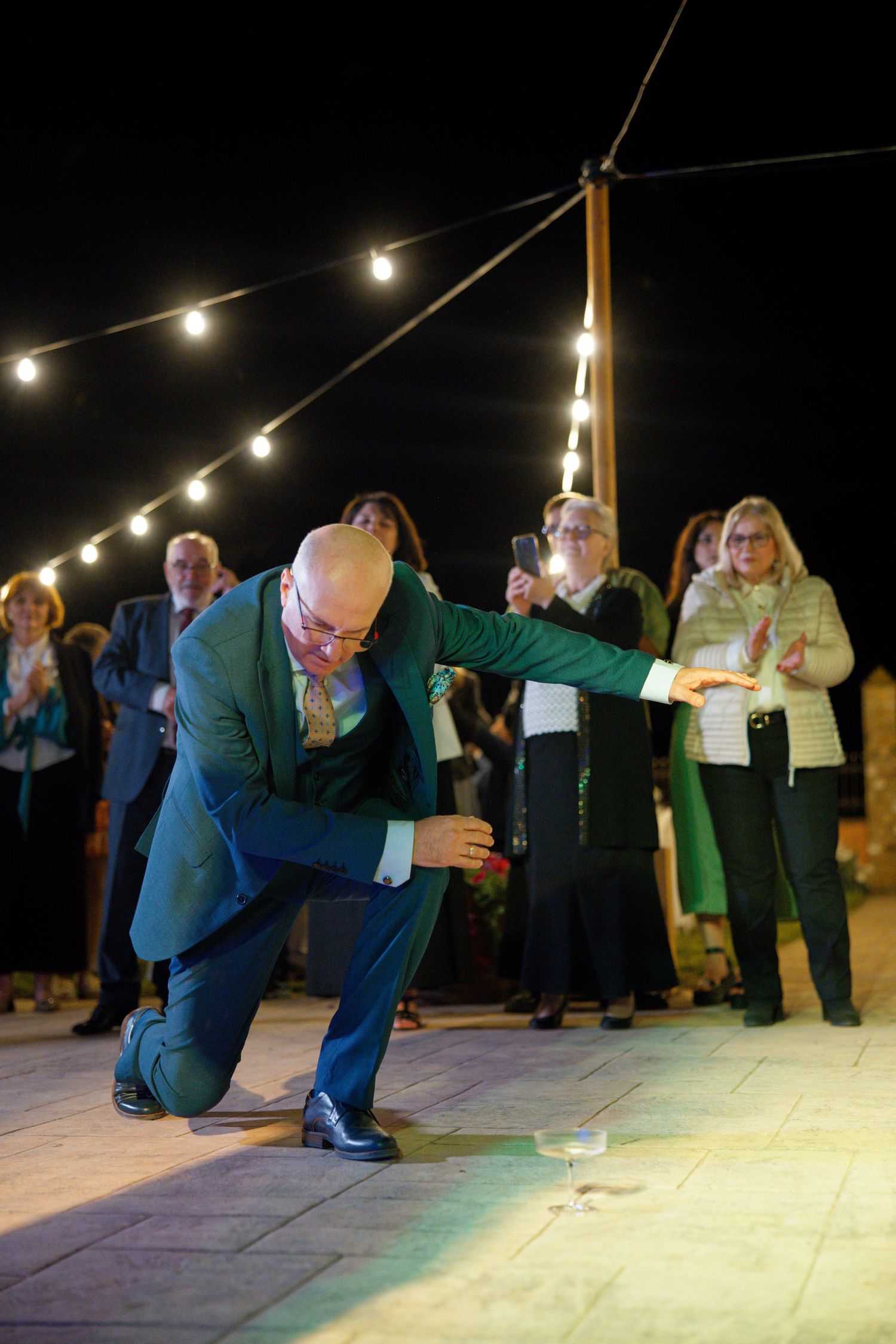 Guests laughing and dancing at a wedding reception under string lights on an outdoor patio.
