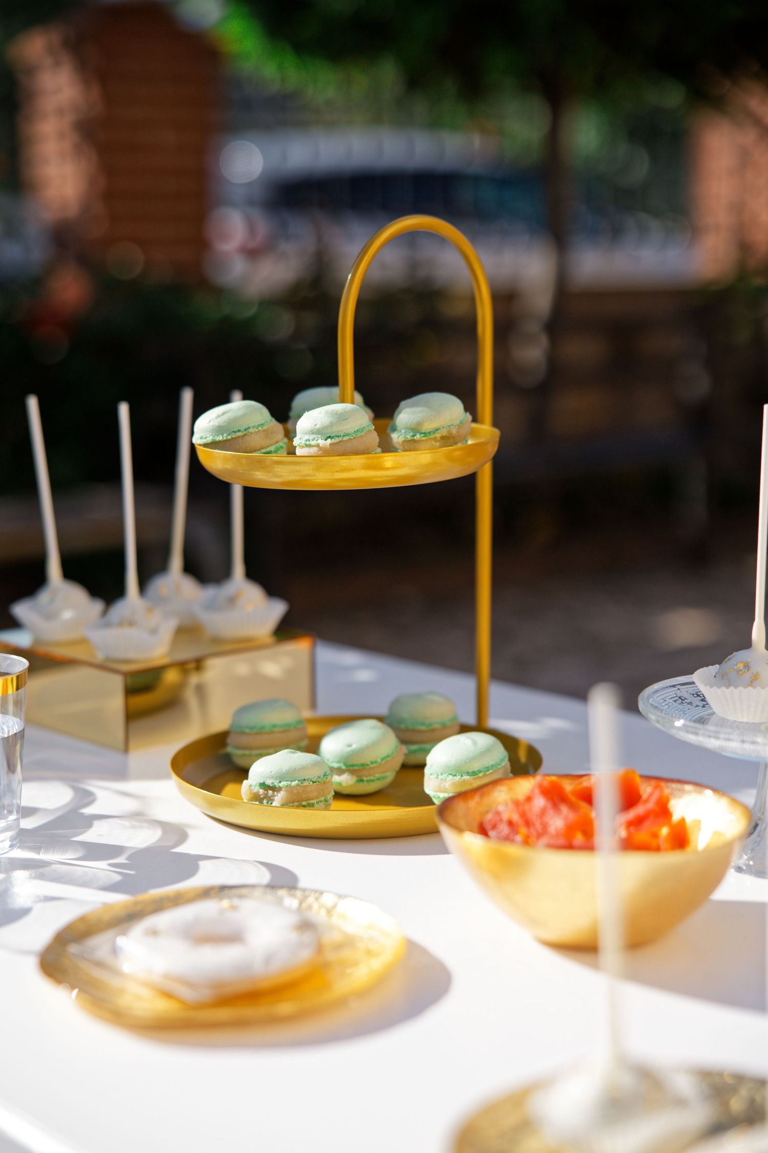 Elegant dessert display featuring macarons on gold tiered stand with appetizers at an outdoor event.