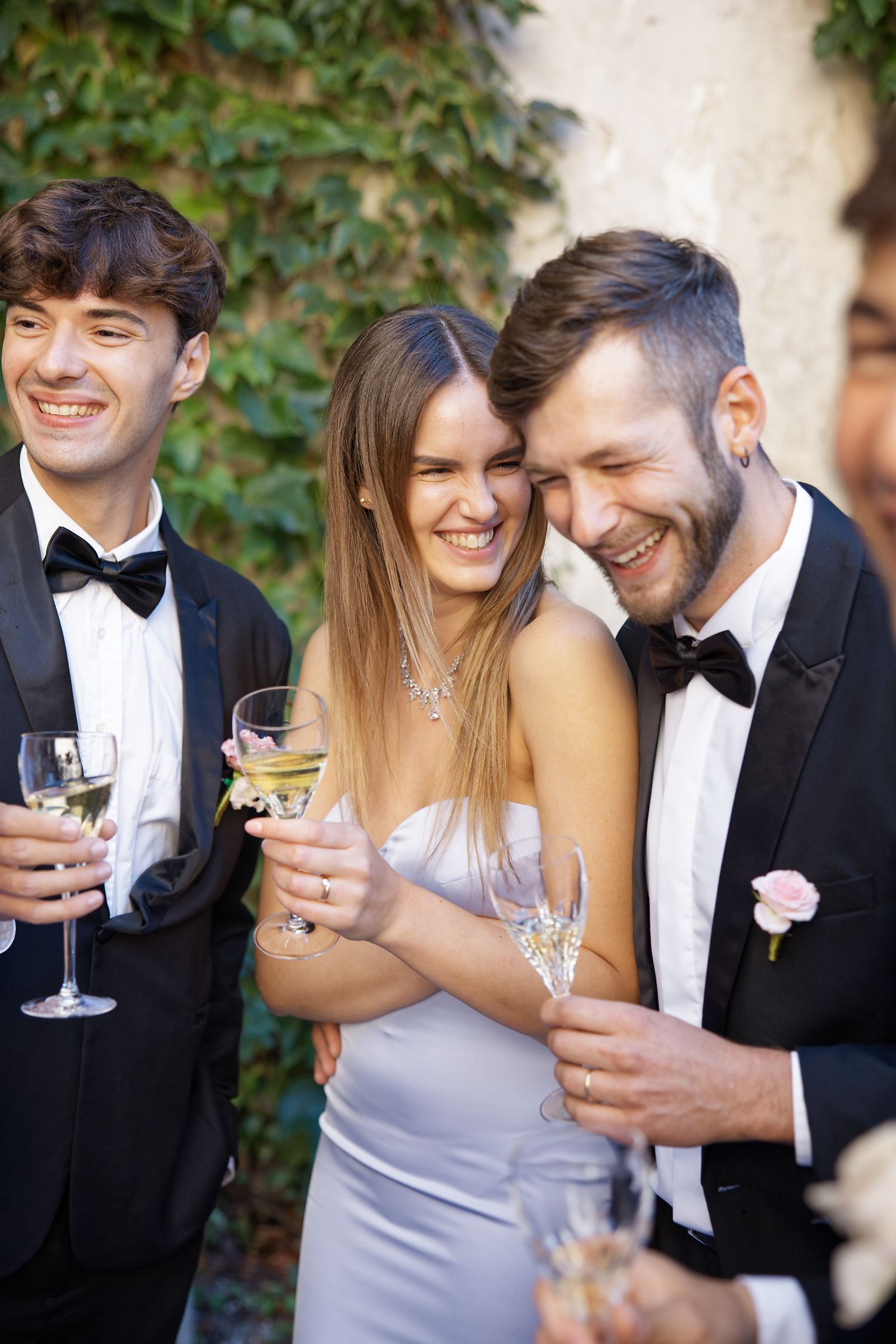 Wedding guests in formal attire sharing champagne and laughter at an outdoor celebration.