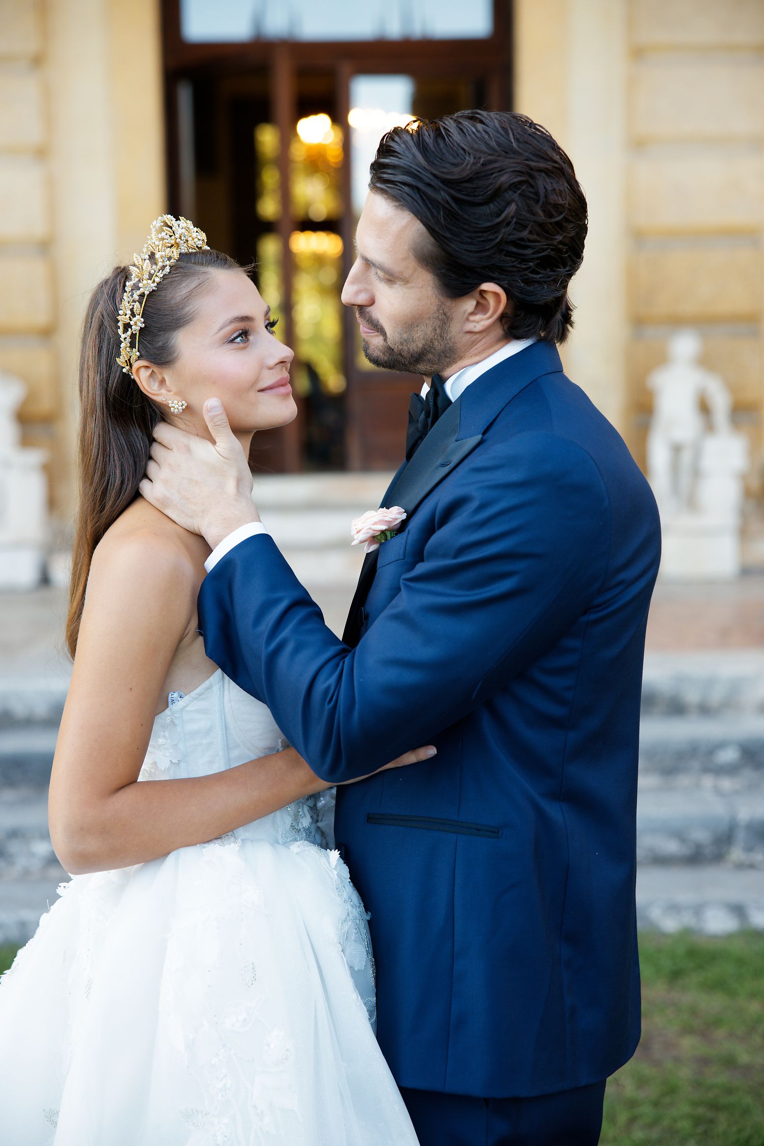 A romantic wedding portrait of a couple sharing an intimate moment against an elegant building exterior.