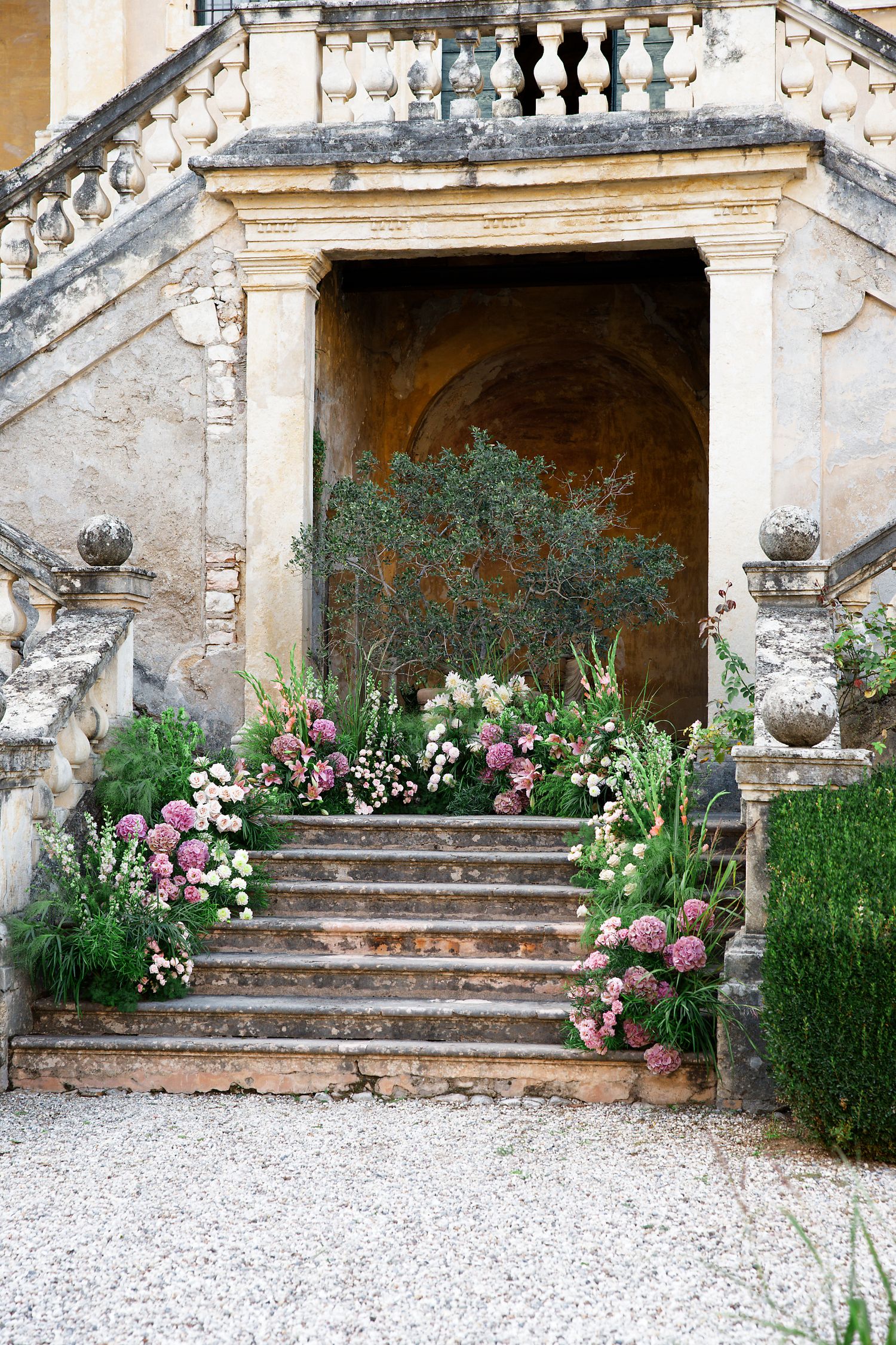 Stone staircase adorned with lush pink and white floral arrangements leading to an arched entrance.