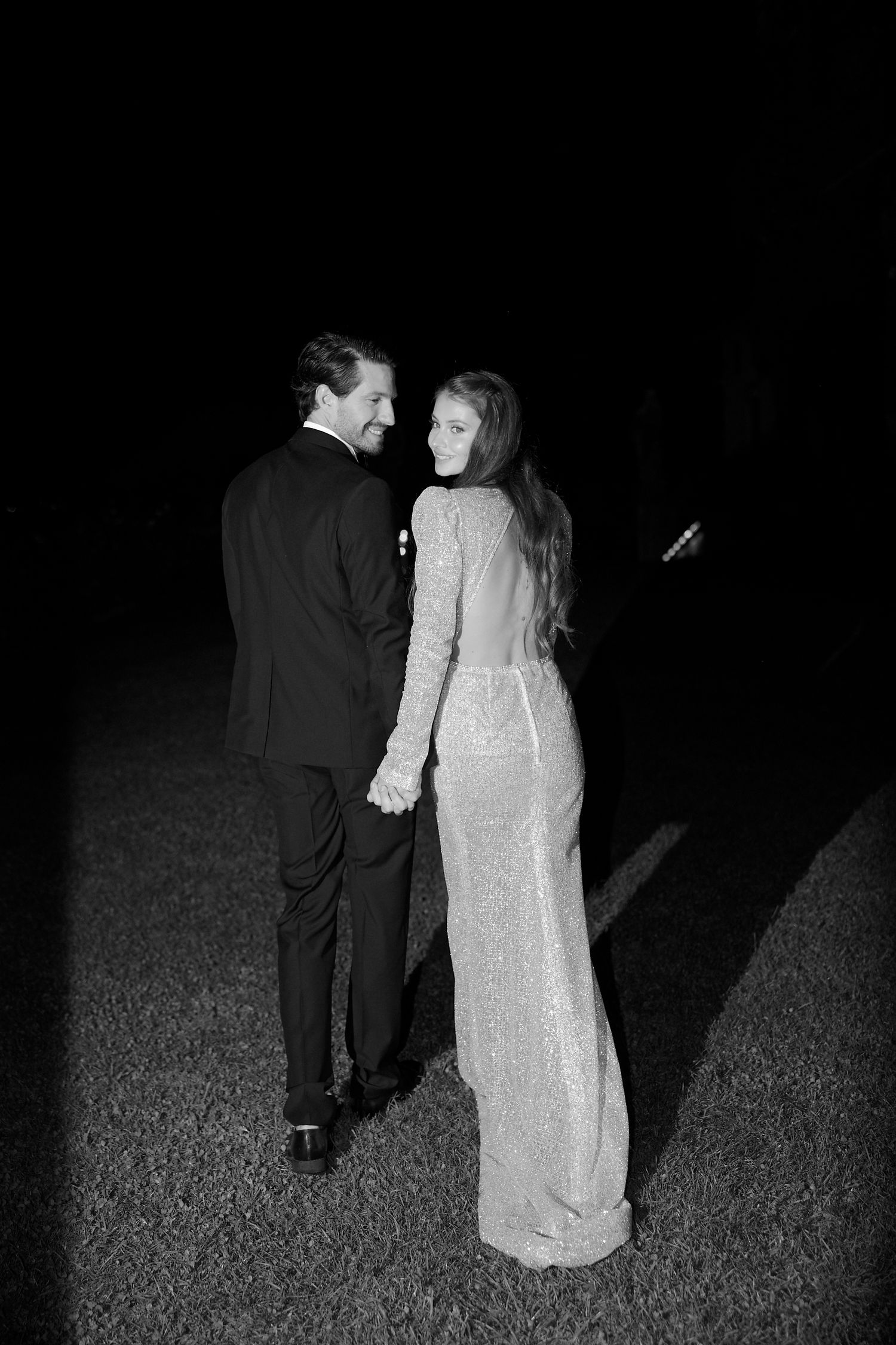 Formal couple sharing private moment on dark lawn during evening event.