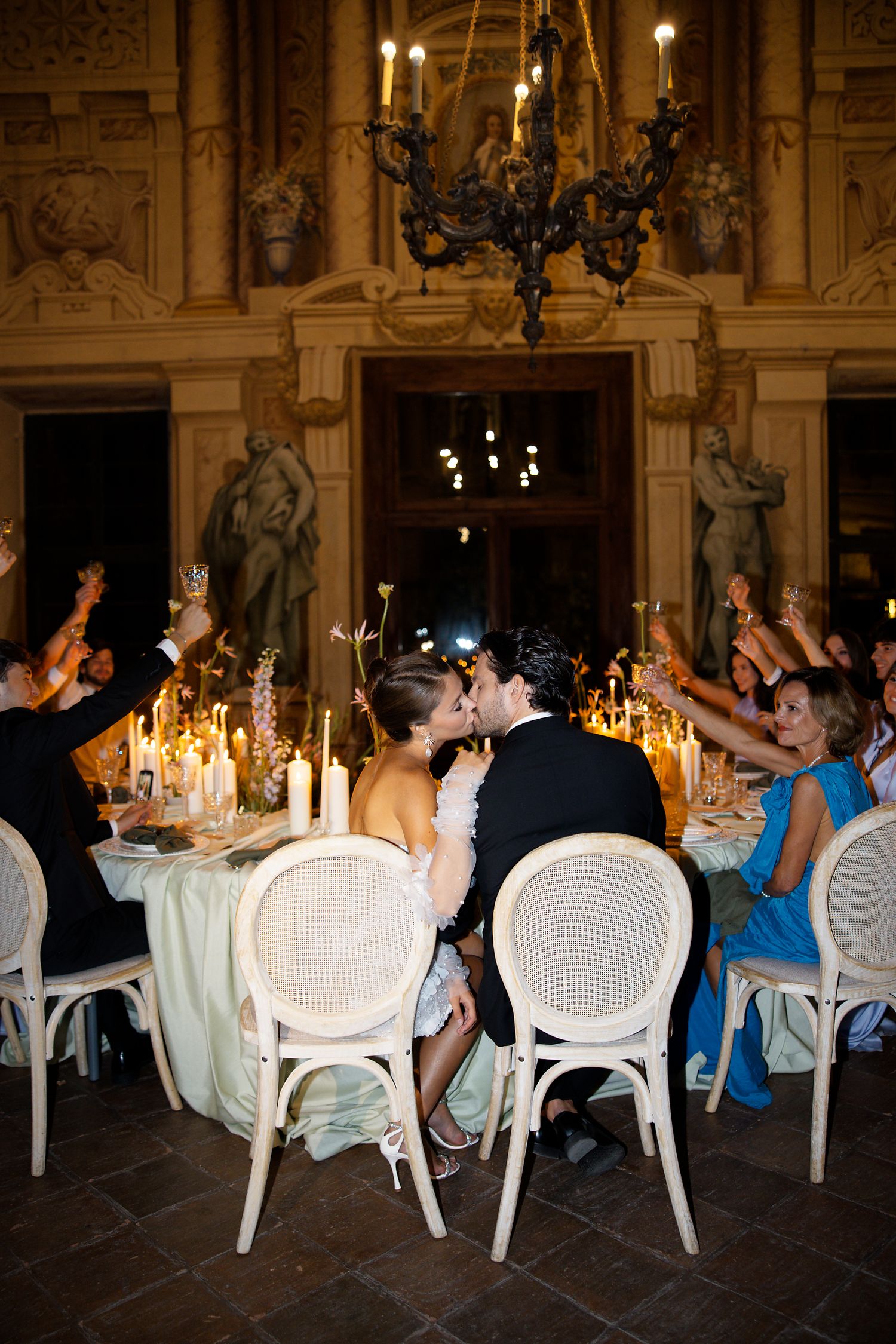 Wedding reception dinner scene with candlelit tables and elegant white chairs in a grand hall.