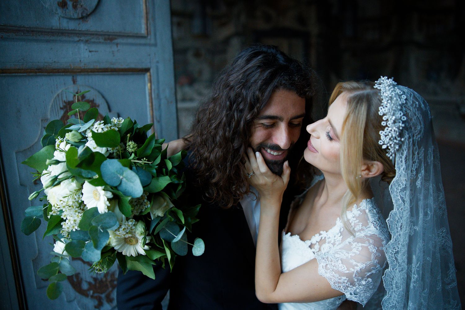 Wedding couple sharing an intimate moment with white bridal bouquet and lace veil details.