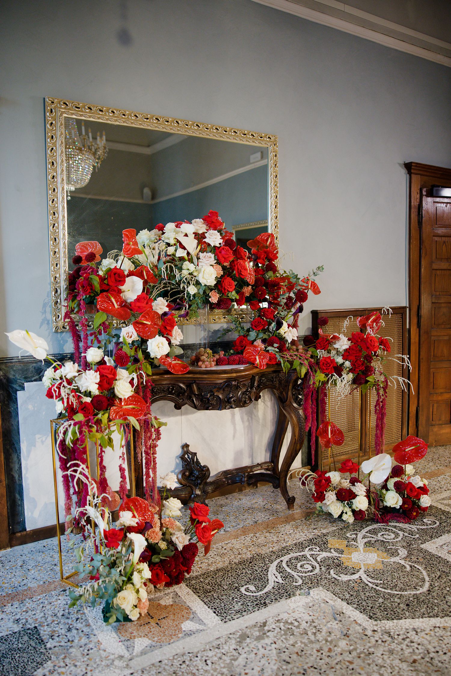 Ornate fireplace decorated with red and white floral arrangements and gold mirror.