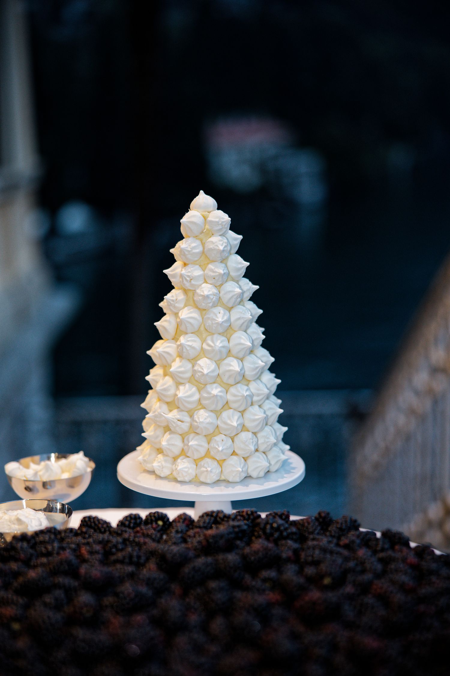 A white cone-shaped wedding cake decorated with meringue kisses sits elegantly on a dark background.