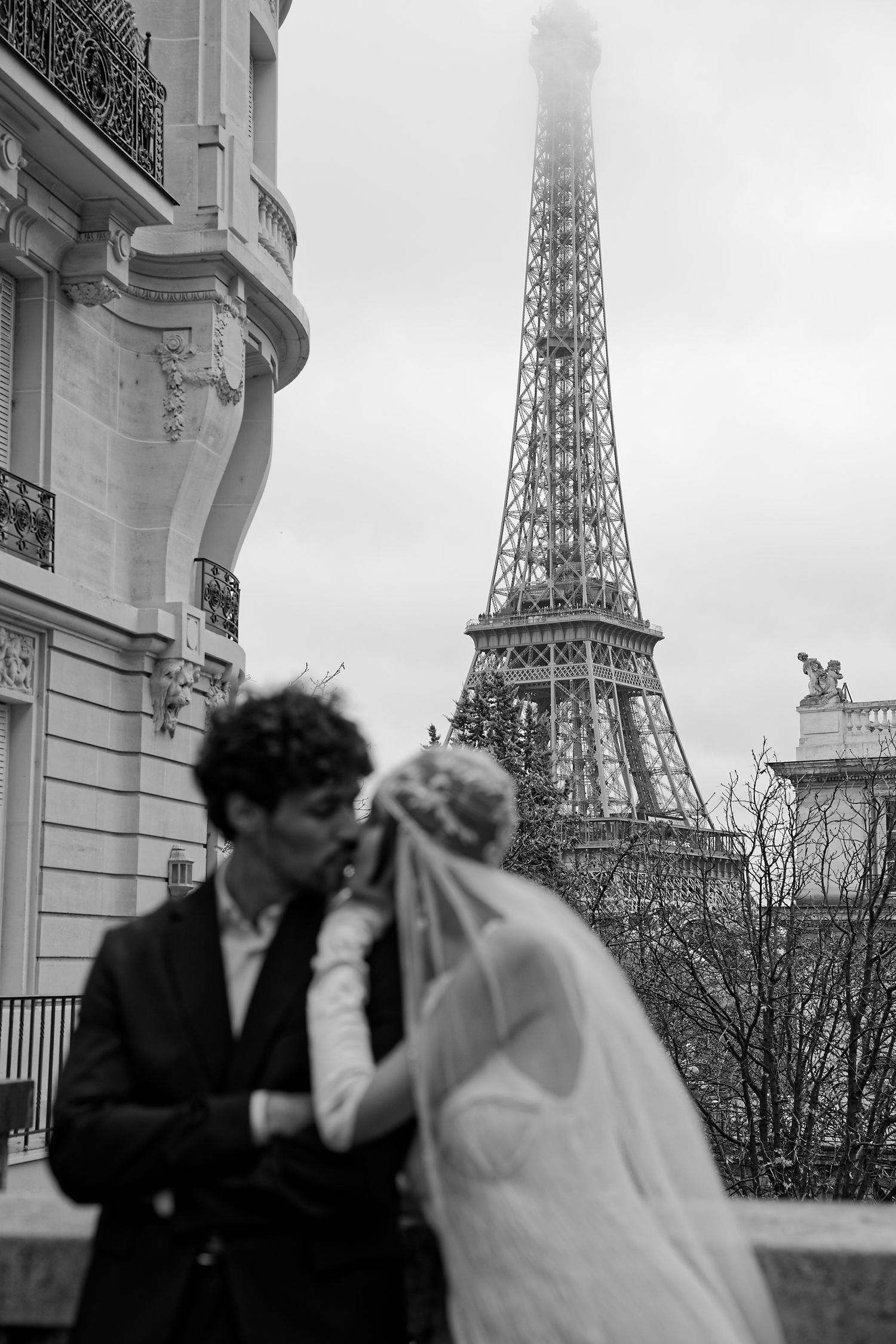 Black and white romantic wedding photo with silhouetted couple kissing against backdrop of Eiffel Tower in Paris.