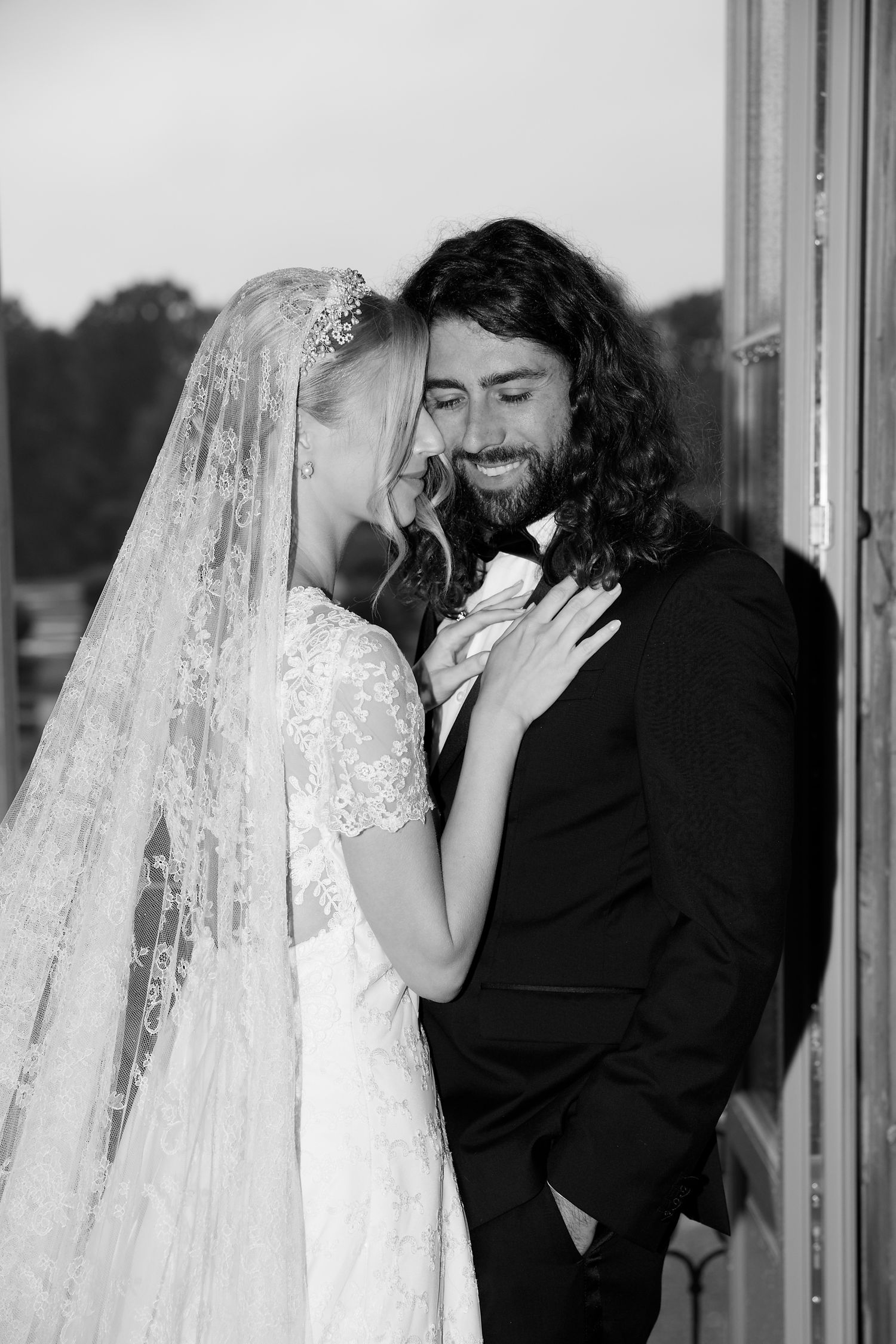 A romantic black and white portrait of newlyweds sharing an intimate moment by a window.