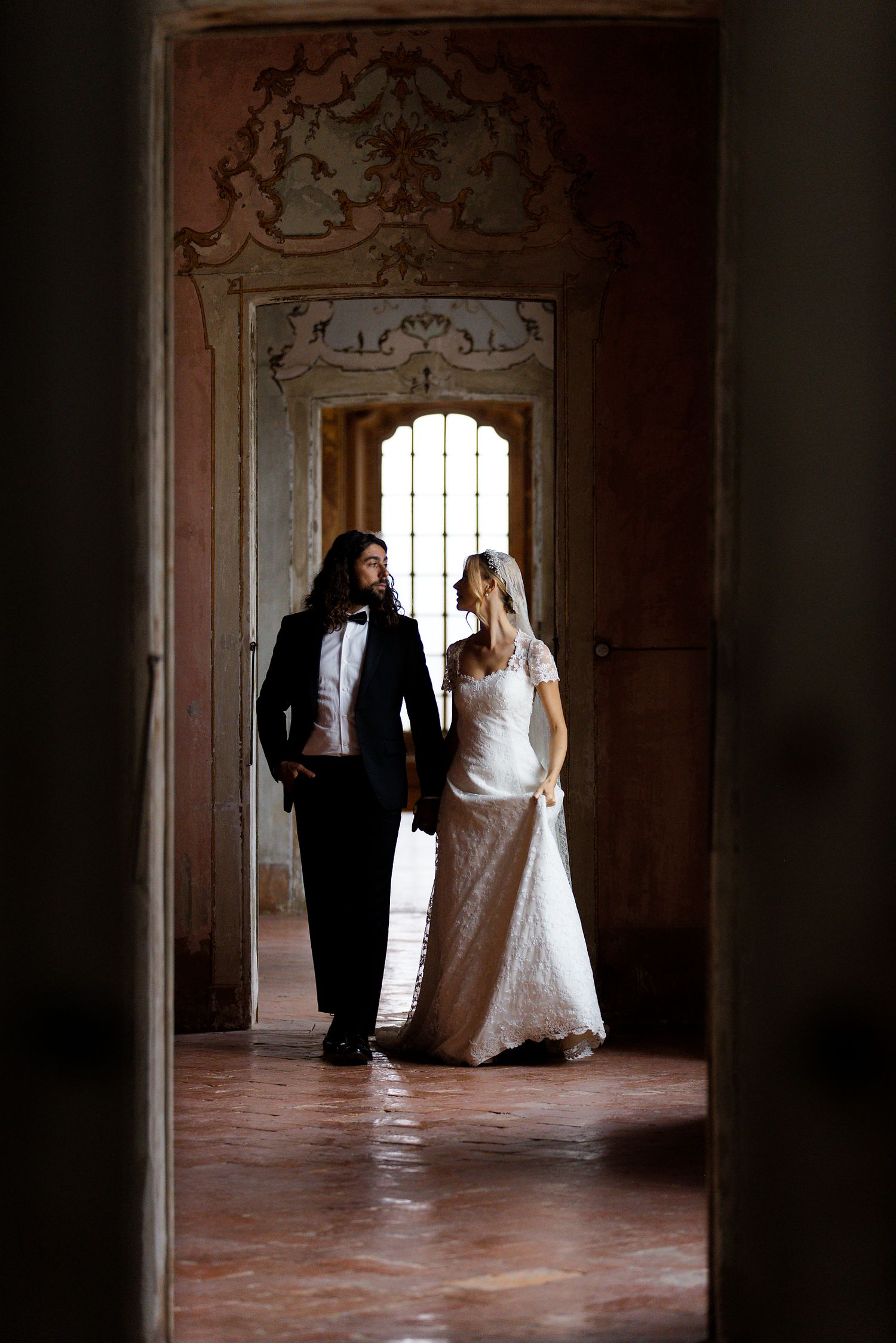 Artistic wedding portrait through an ornate doorframe showing a couple in formal attire.