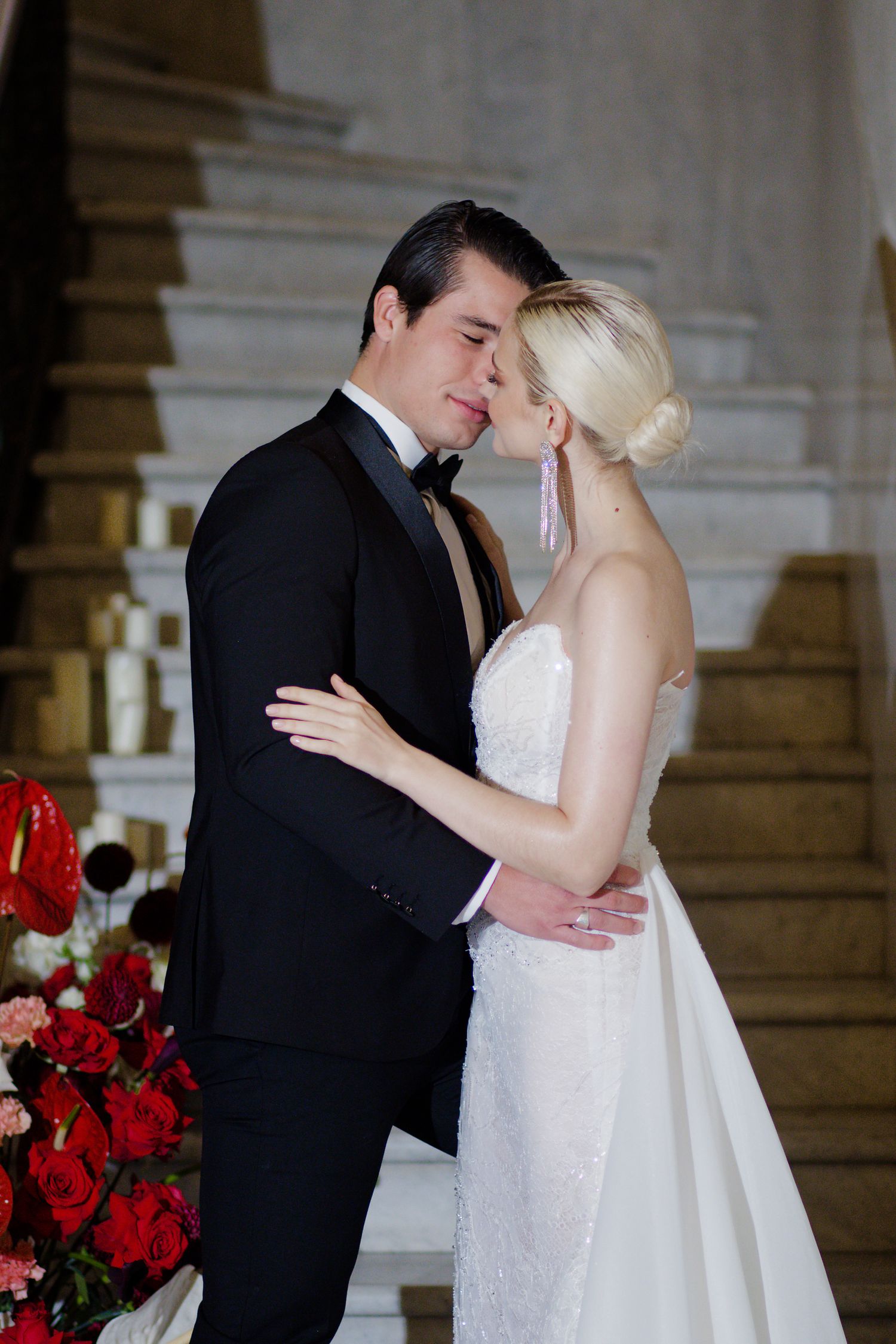 An intimate wedding moment captured on a staircase with red roses in the foreground.
