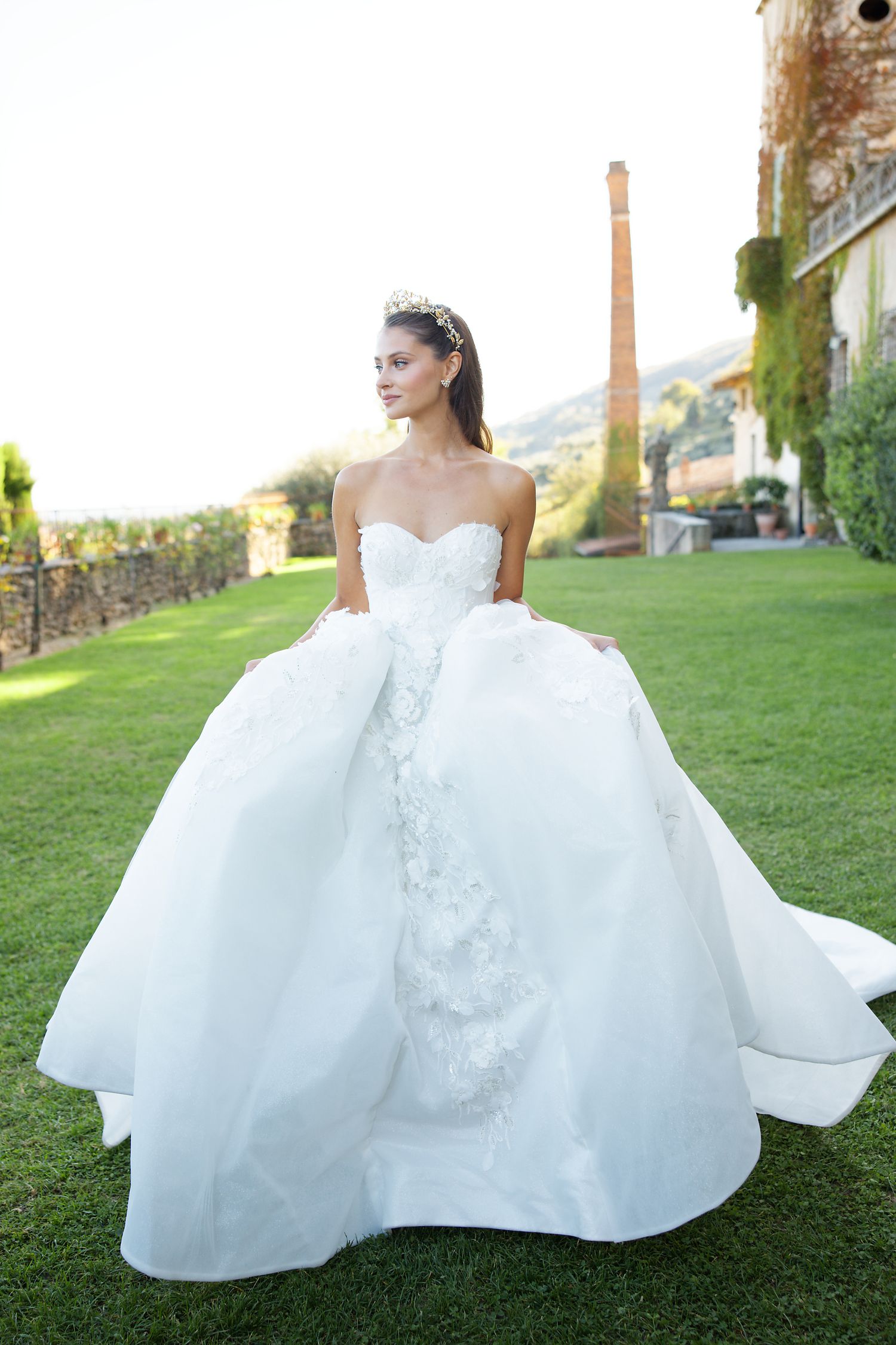 A stunning bridal portrait featuring a voluminous white ball gown on manicured garden grounds.