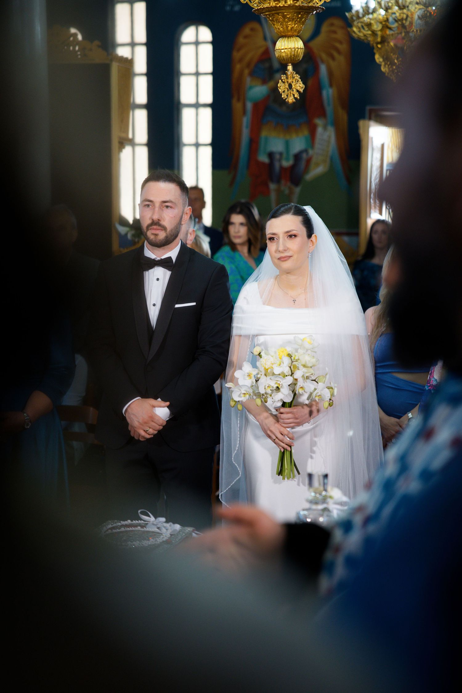 The wedding ceremony takes place in an ornate church with tall windows and elegant chandeliers.