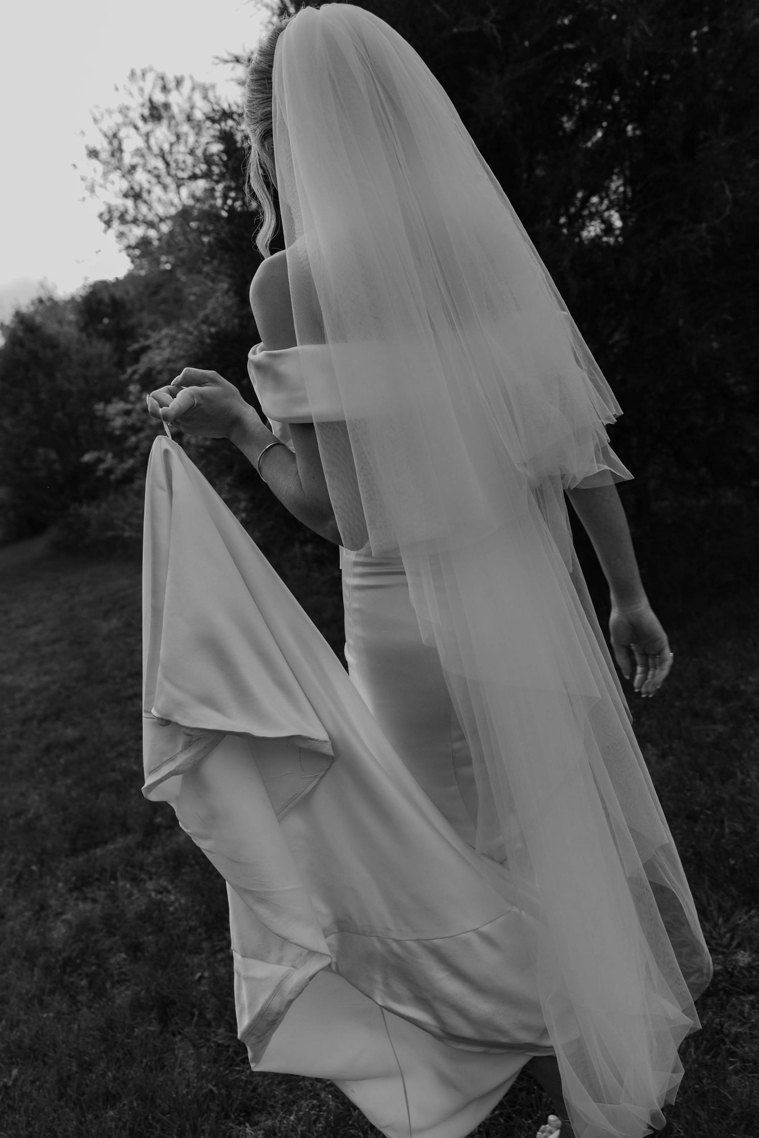 Birmingham Alabama Photographer capturing bride holding her dress walking in a field, at Iris Woods Venue in Nashville, Tennessee