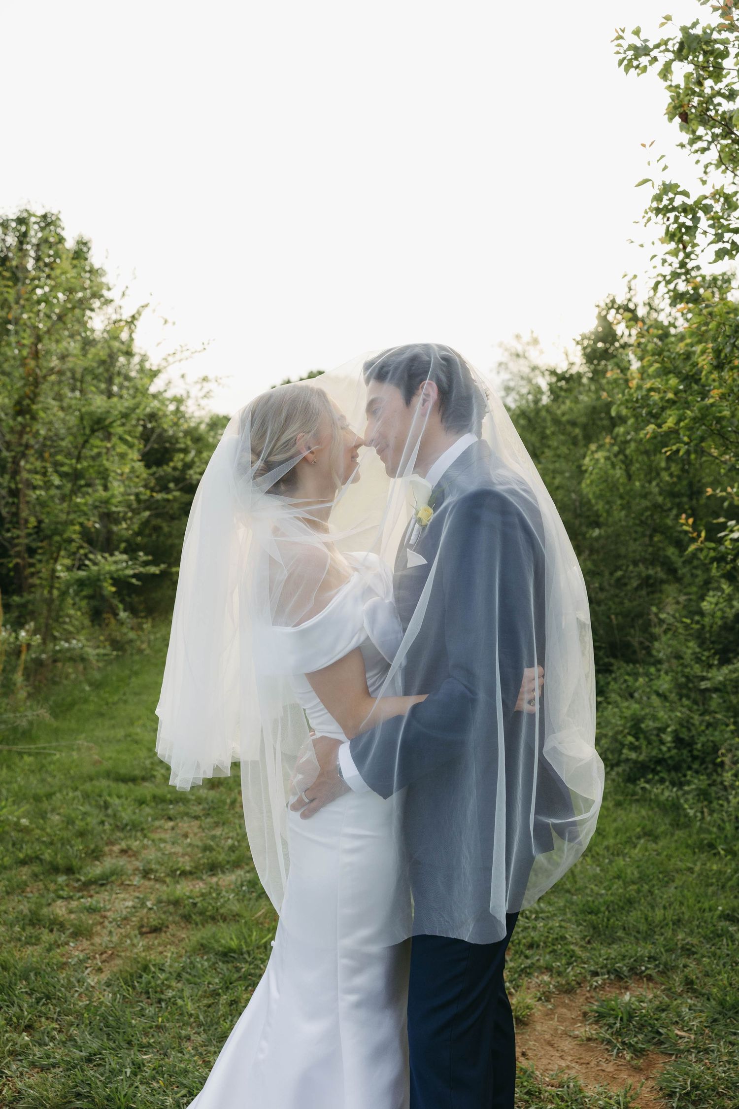 Birmingham Alabama Photographer capturing bride and groom posing under the veil, in a field, at Iris Woods Venue in Nashville, Tennessee