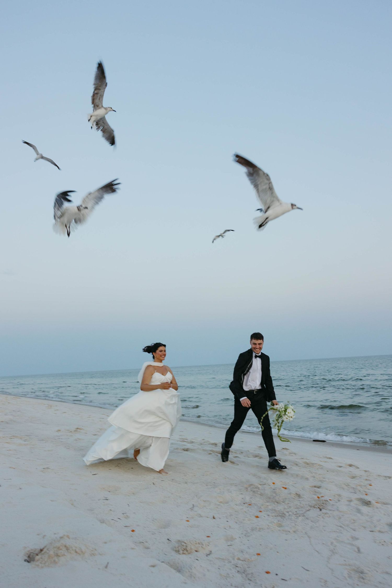 Birmingham Alabama Photographer capturing Bride and groom running on the beach with seagulls, at gulf shores beach in Alabama