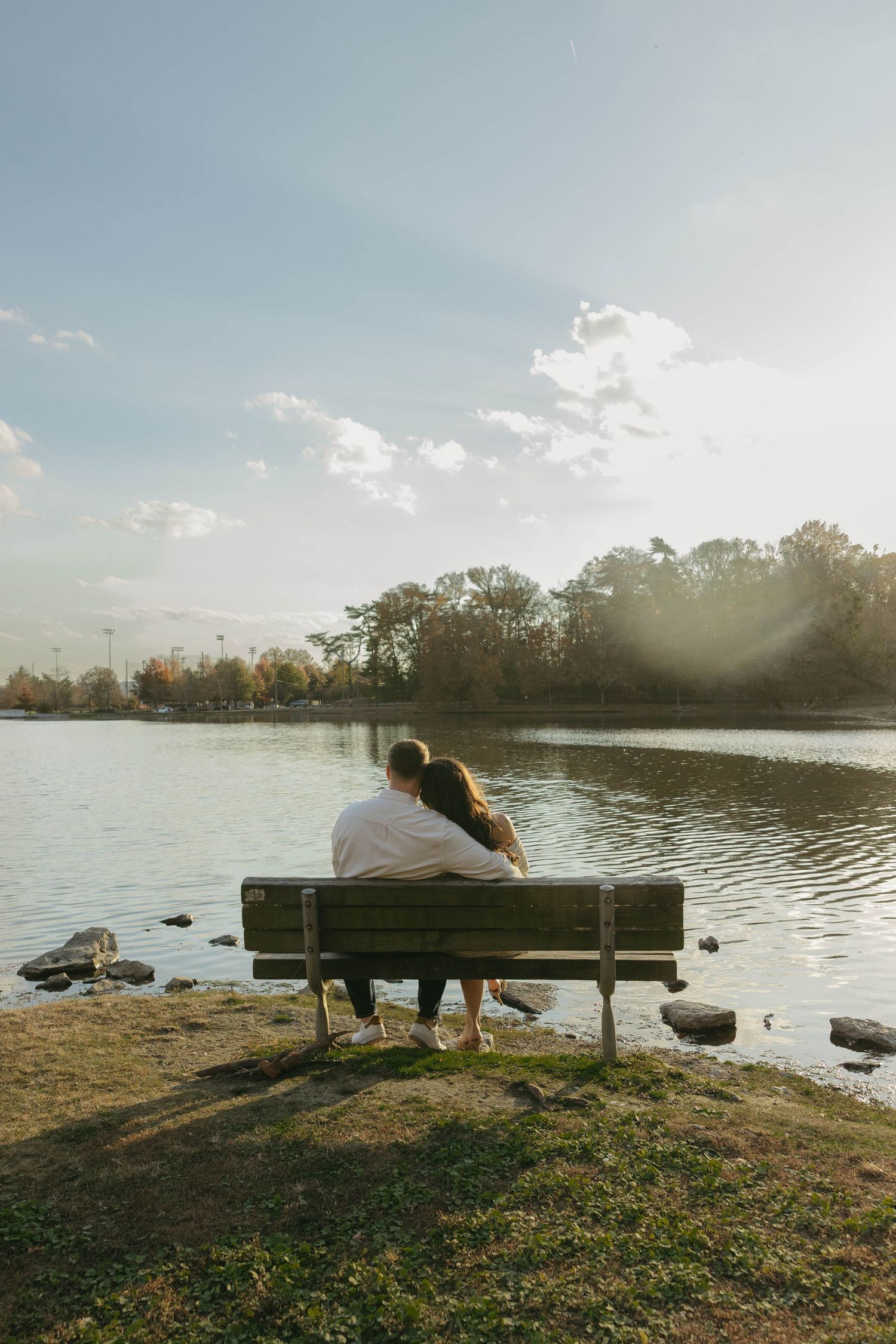 Birmingham Alabama Photographer capturing an engagement session of a couple hugging on a bench in a park by a lake in Nashville Tennessee