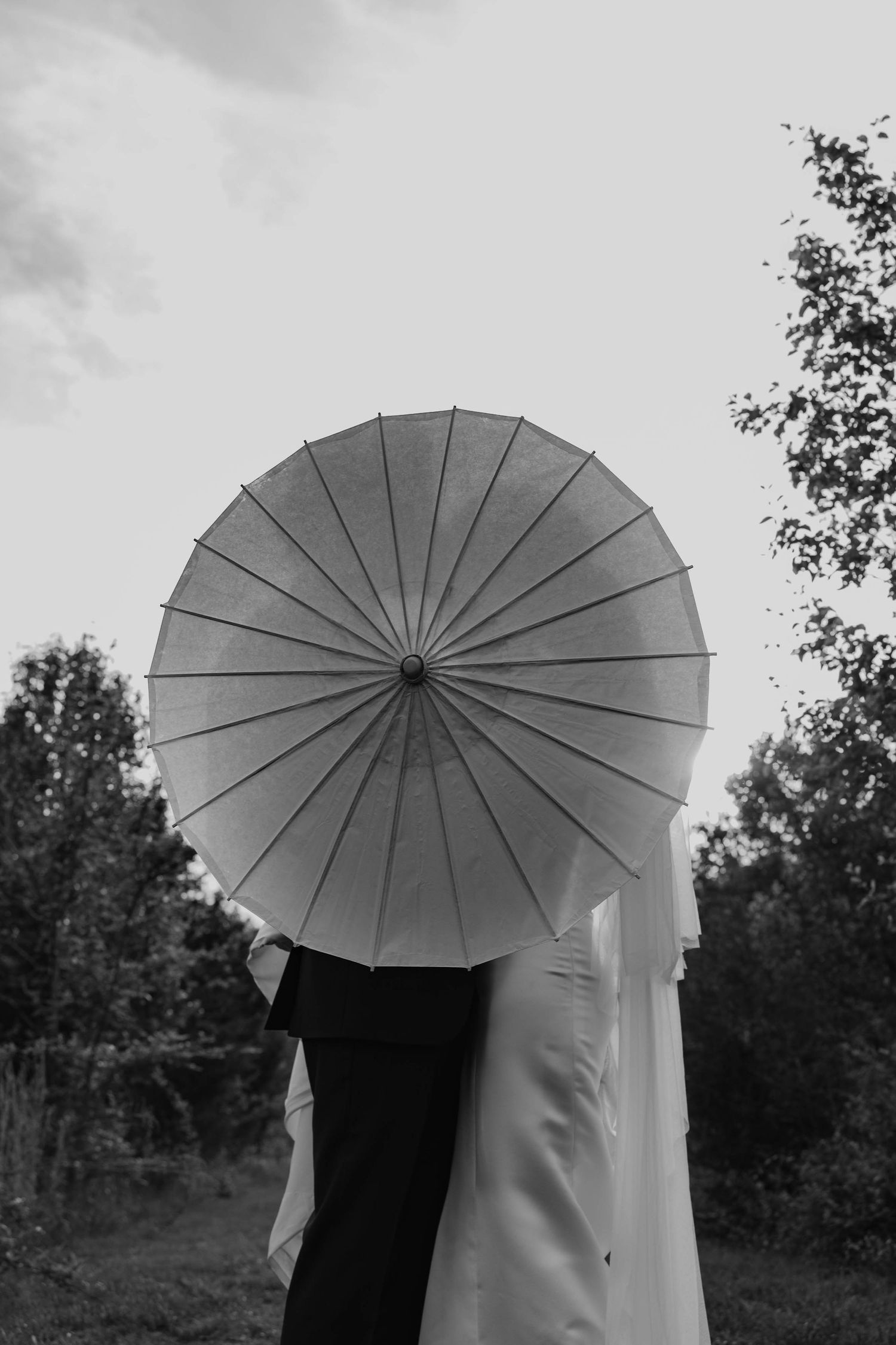 Birmingham Alabama Photographer capturing bride and groom kissing behind a parasol, in a field, at Iris Woods Venue in Nashville, Tennessee