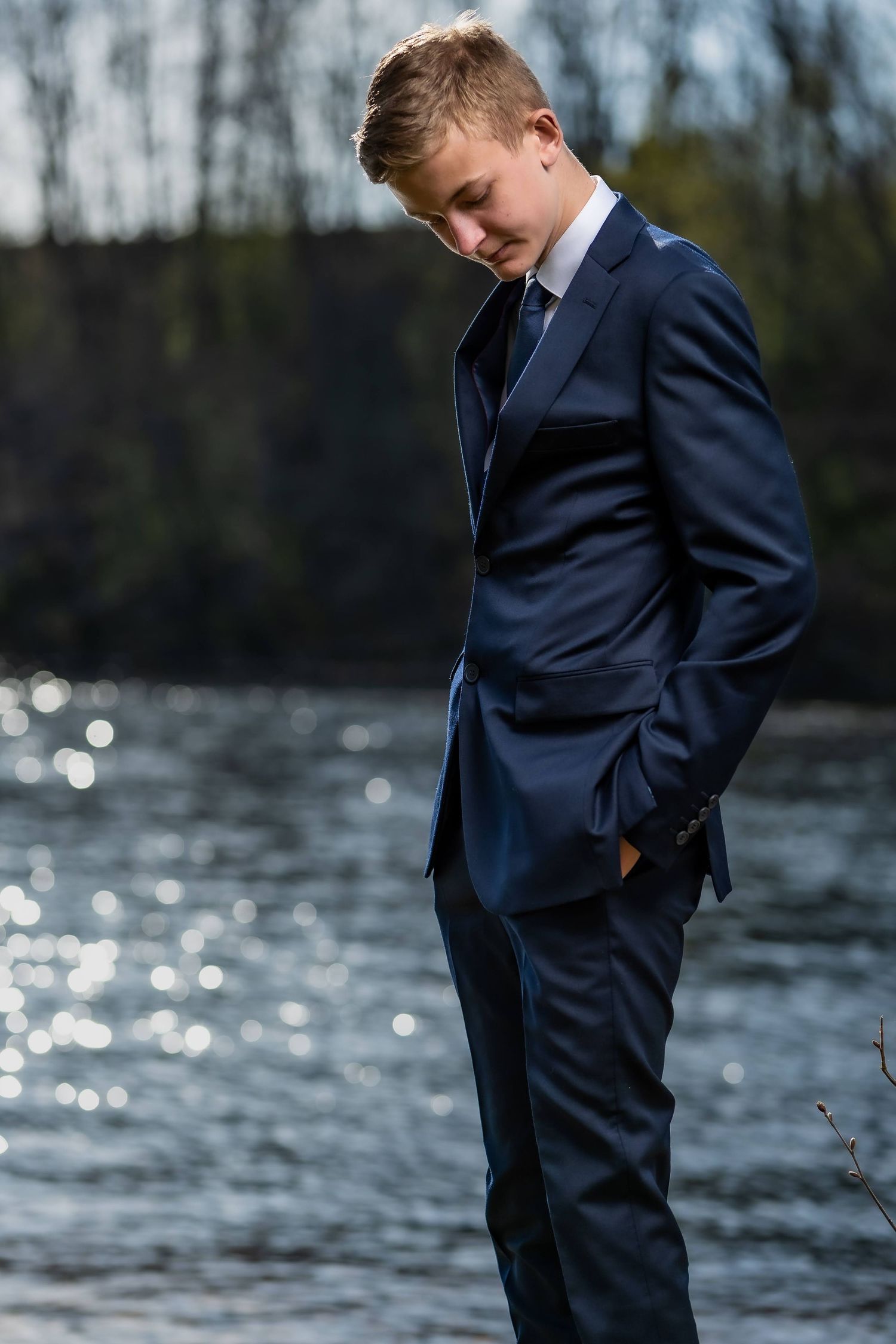Portrettfoto – gutt i marineblå dress ved solbelyst innsjø, konfirmant
