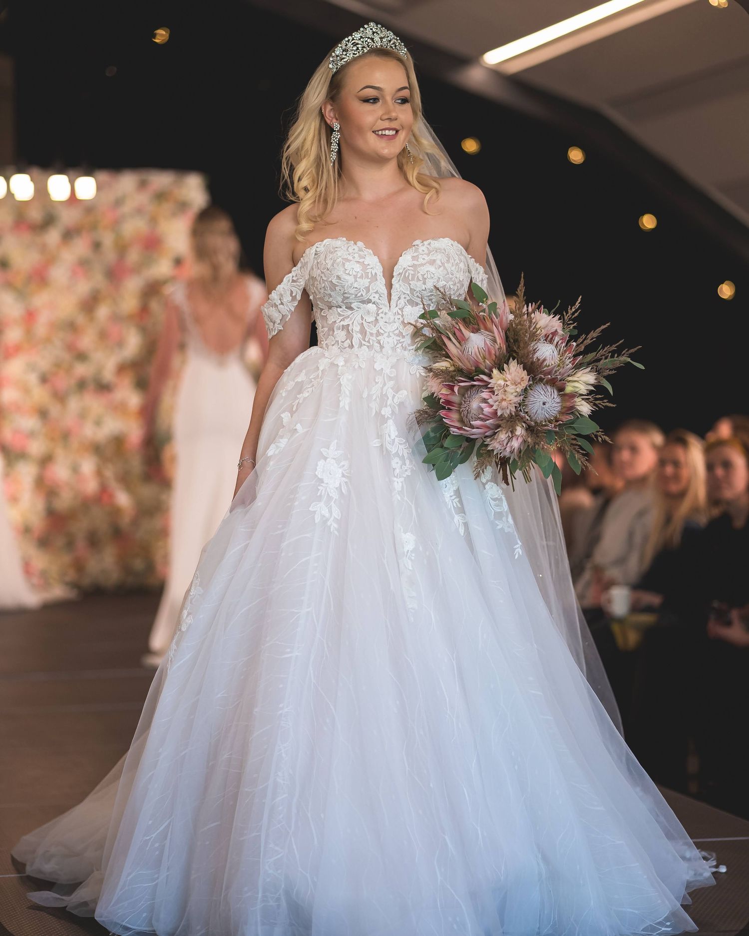 Brudekjole på catwalk – off shoulder-kjole med blonder og blomsterbukett
