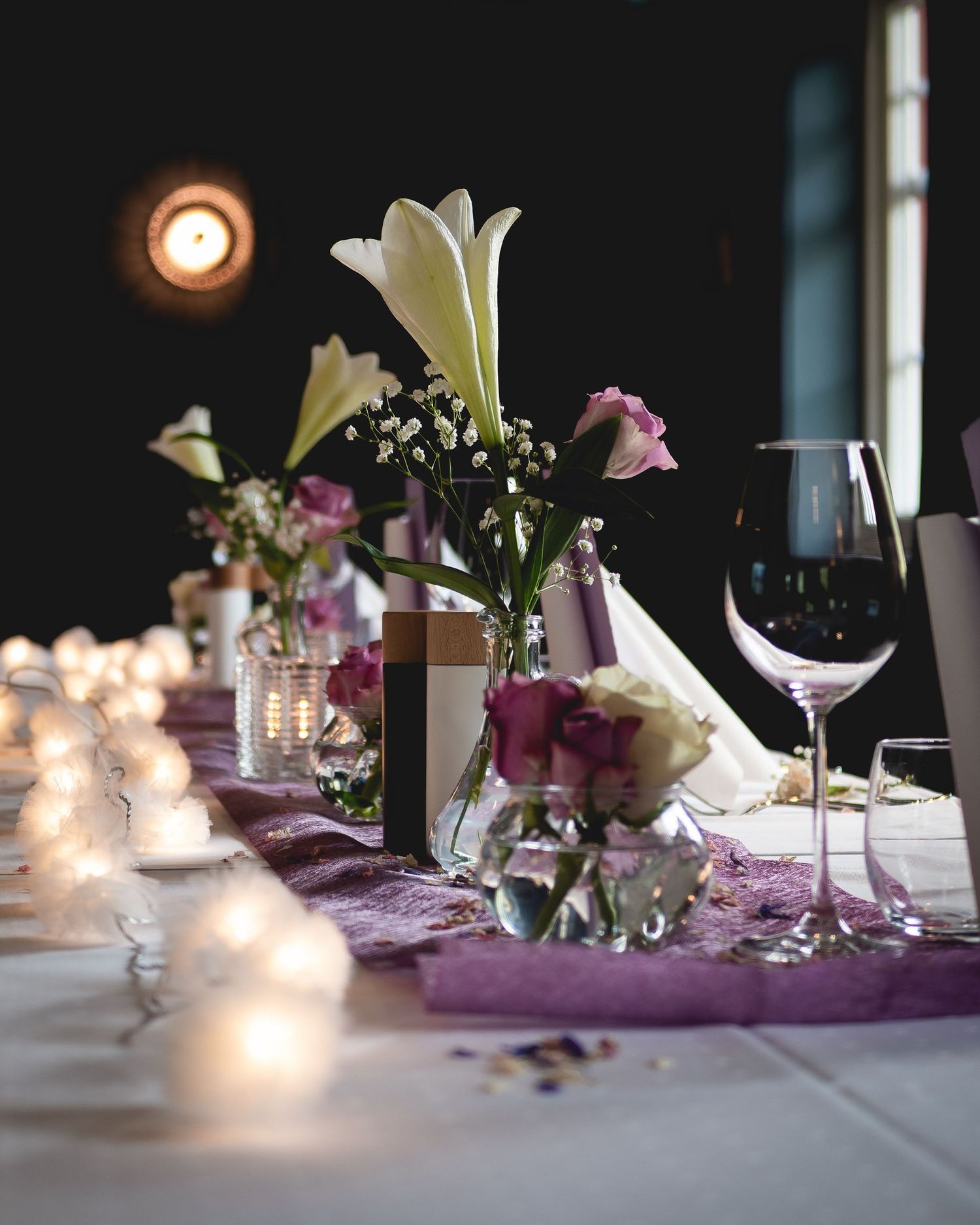 Borddekorasjon – blomsteroppsats med liljer og roser i stemningsfull belysning