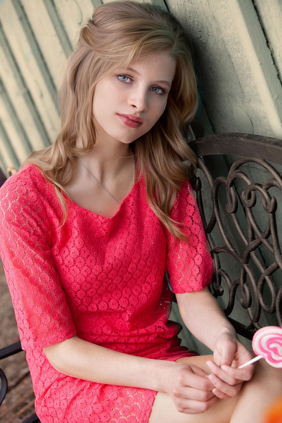Senior girl in pink lace dress holding a lollipop while sitting on a decorative bench outdoors, by Jocelyn M. Photography in Rochester, MI