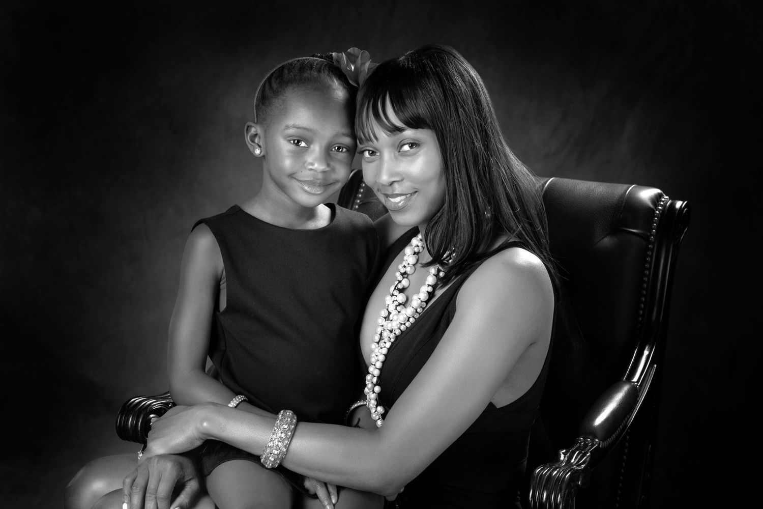 Black and white portrait of a woman and young girl in elegant attire, seated together in a studio setting.