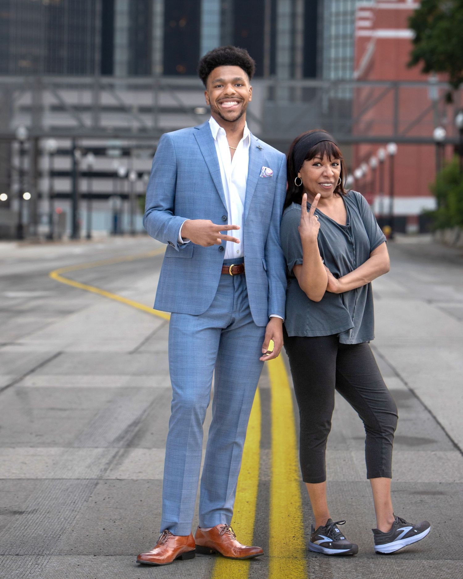 Tall young man in blue suit poses with woman in casual attire on urban street with yellow line.