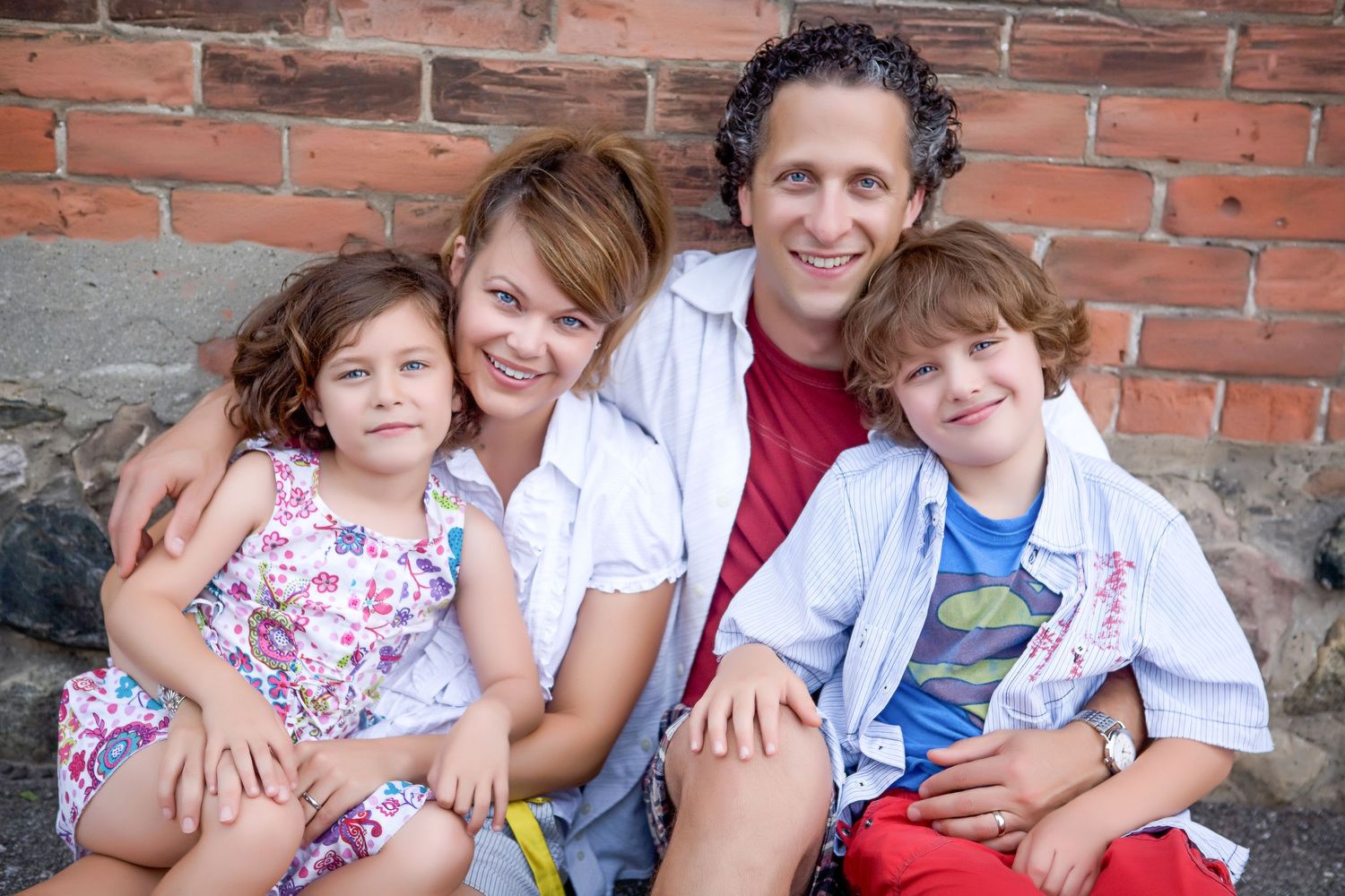 Happy family of four smiling together against a brick wall outdoors.