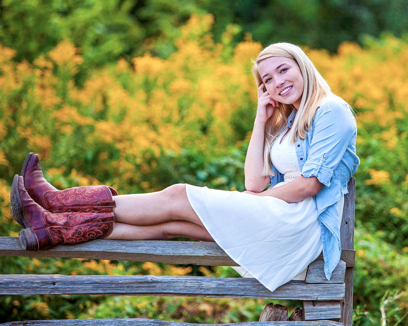 Senior girl portait sitting on a wooden fence with yellow flowers, by Jocelyn M. Photography in Rochester, MI