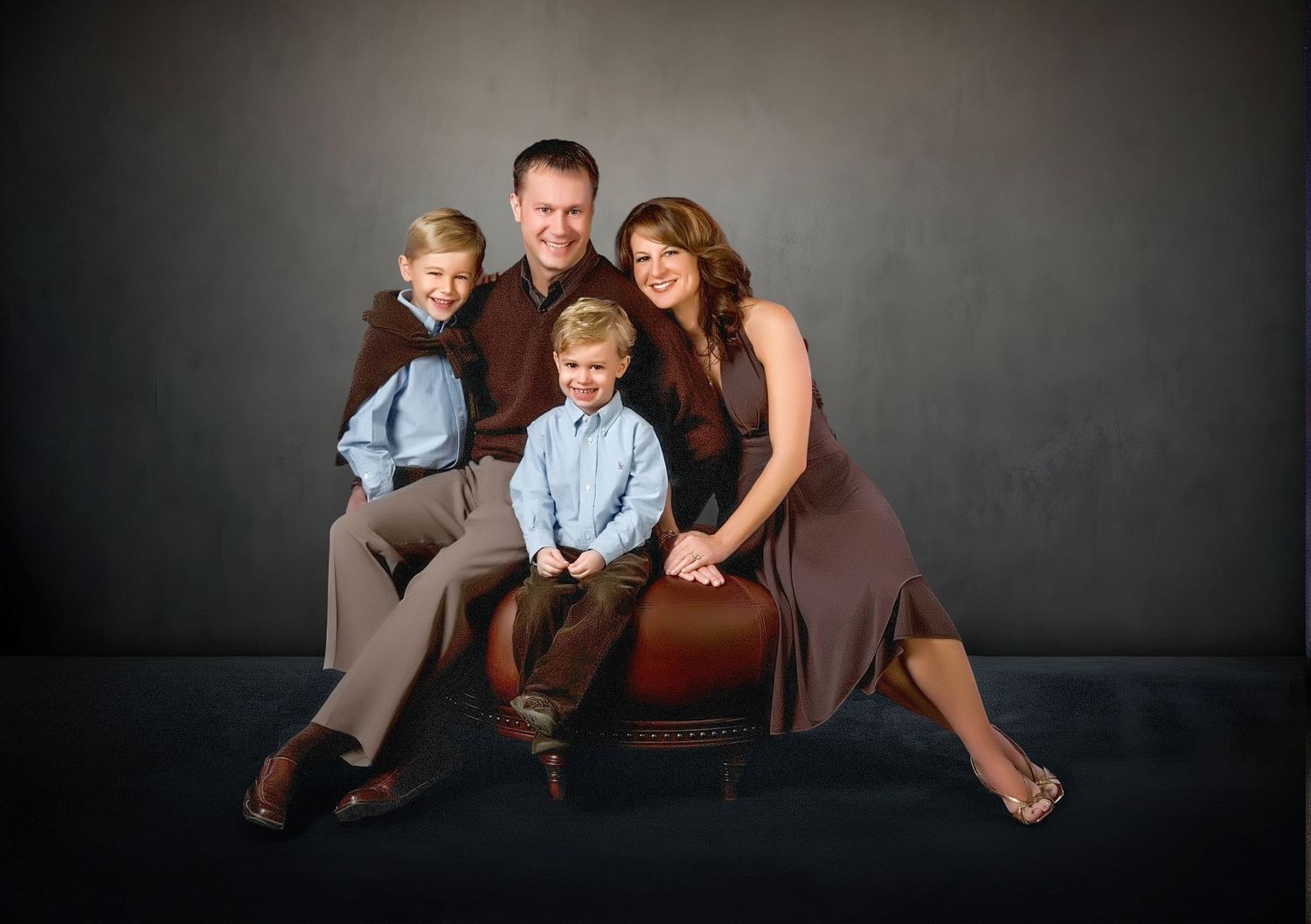 Happy family of four poses together on studio ottoman for professional family portrait.