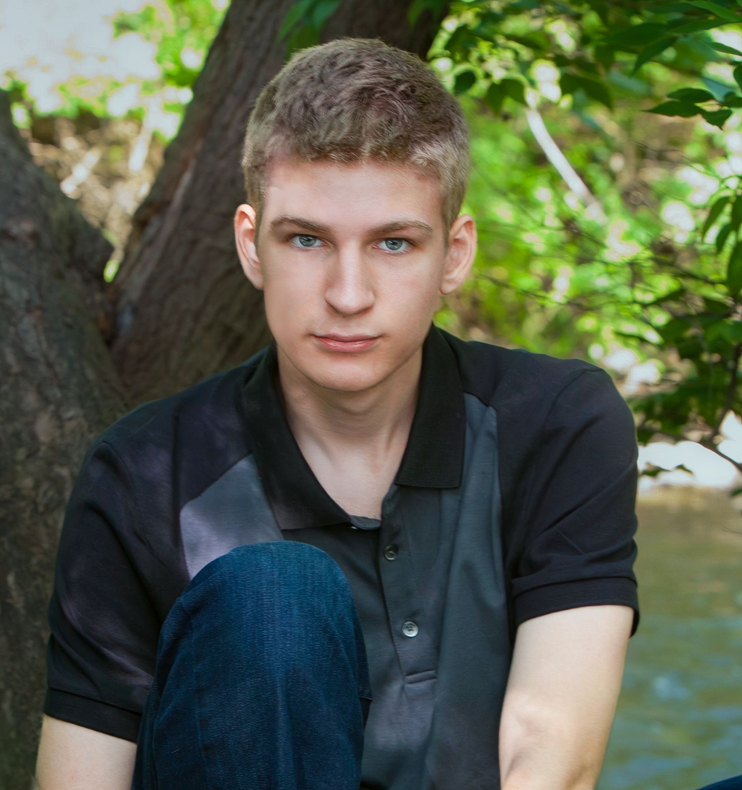Young man sitting outdoors against a tree in natural light, by Jocelyn M. Photography in Rochester, MI