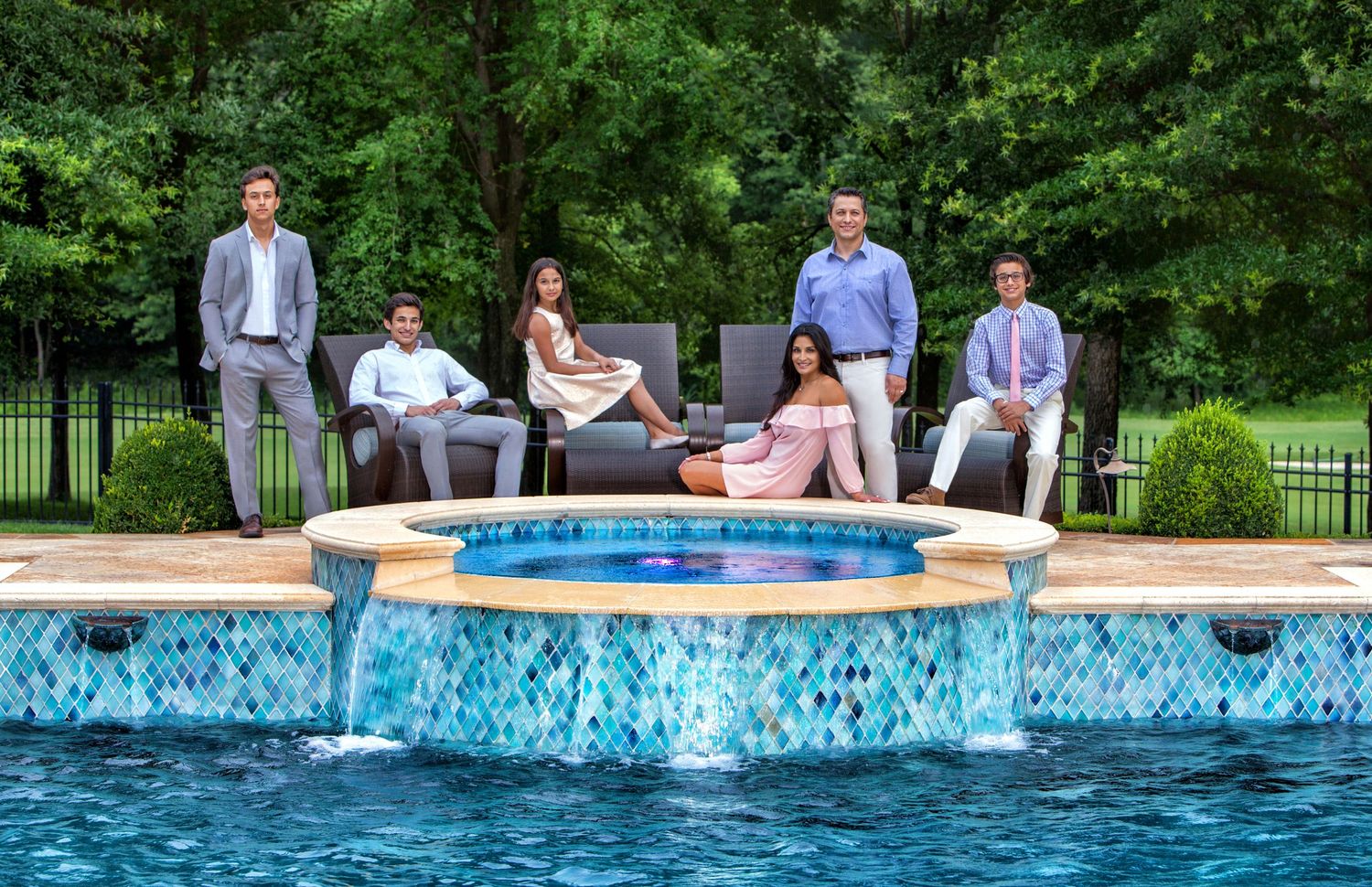 Family group photo by a luxury pool with waterfall feature, surrounded by lush greenery.