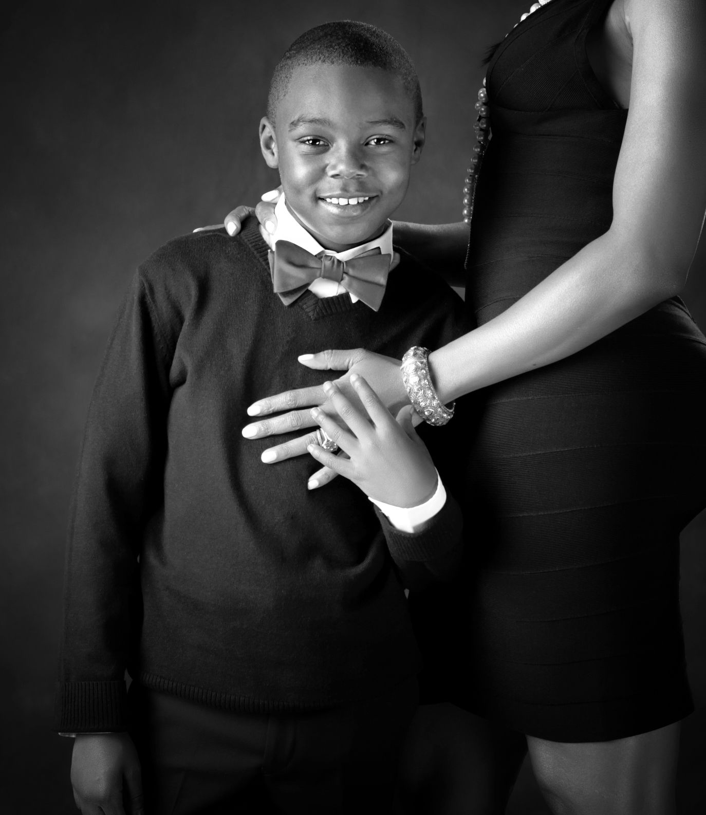 Black and white portrait of a smiling boy in bow tie suit with a woman beside him.