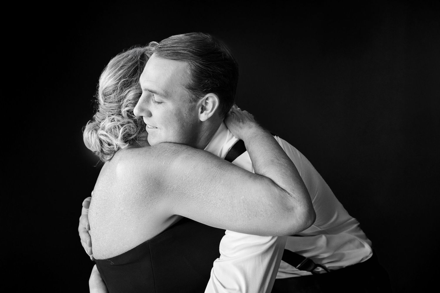 Black and white photo of a man and woman sharing a tender embrace against a dark background.