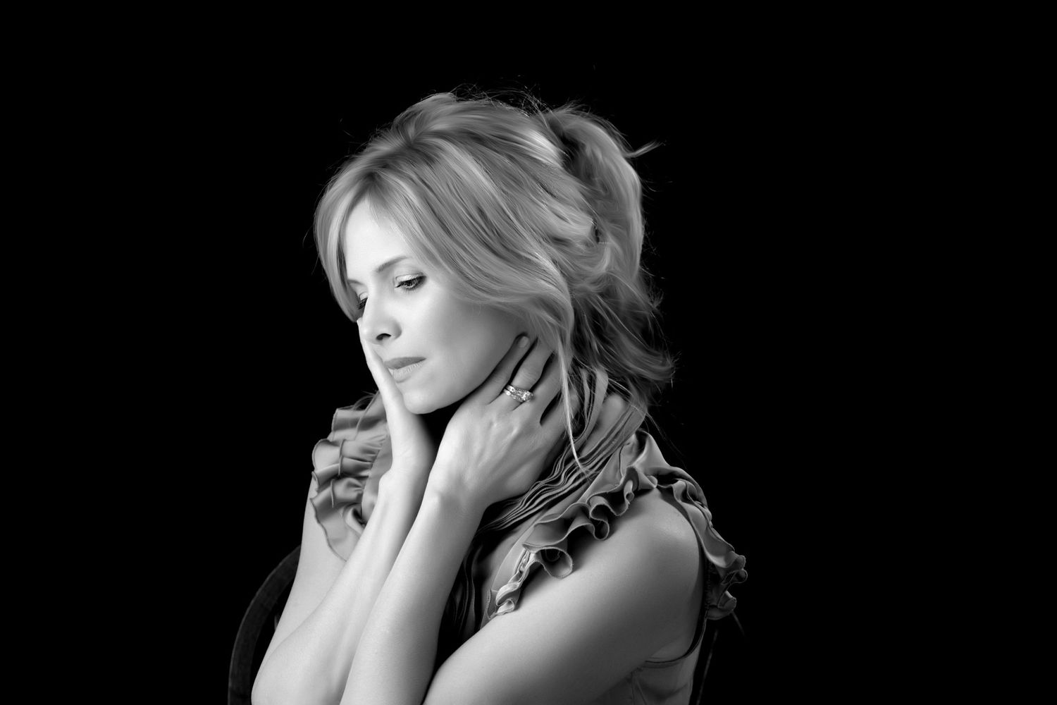 Black and white portrait of a blonde woman with eyes closed touching her neck gracefully.